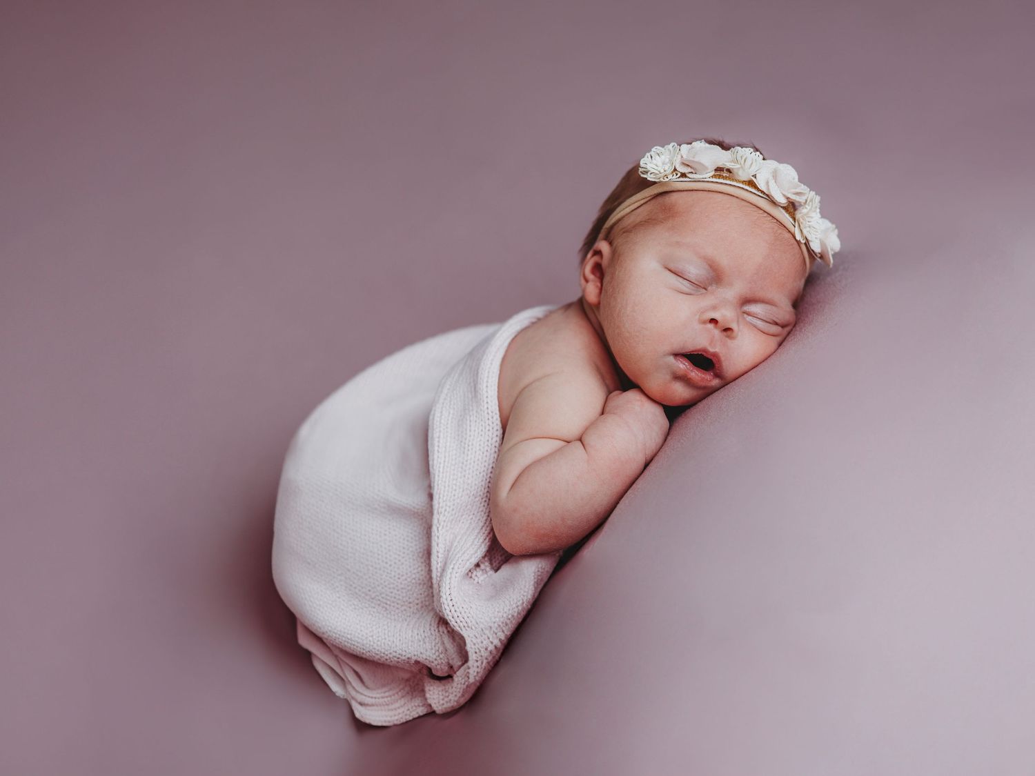 Newborn baby wrapped in soft white blanket sleeping peacefully in studio lighting.