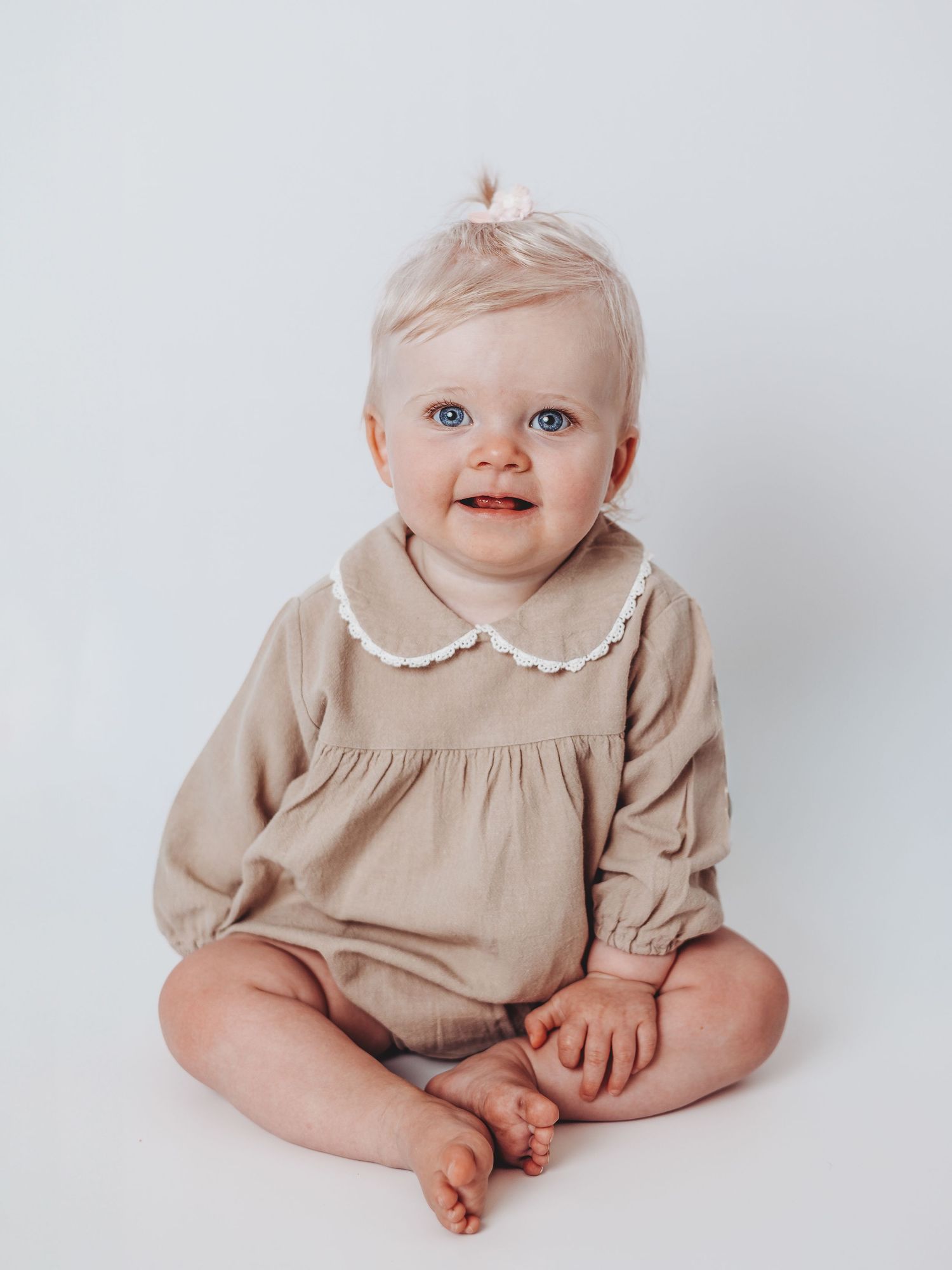 A baby wearing a beige dress sits on a white background in a series of connected photos showing different poses and angles.