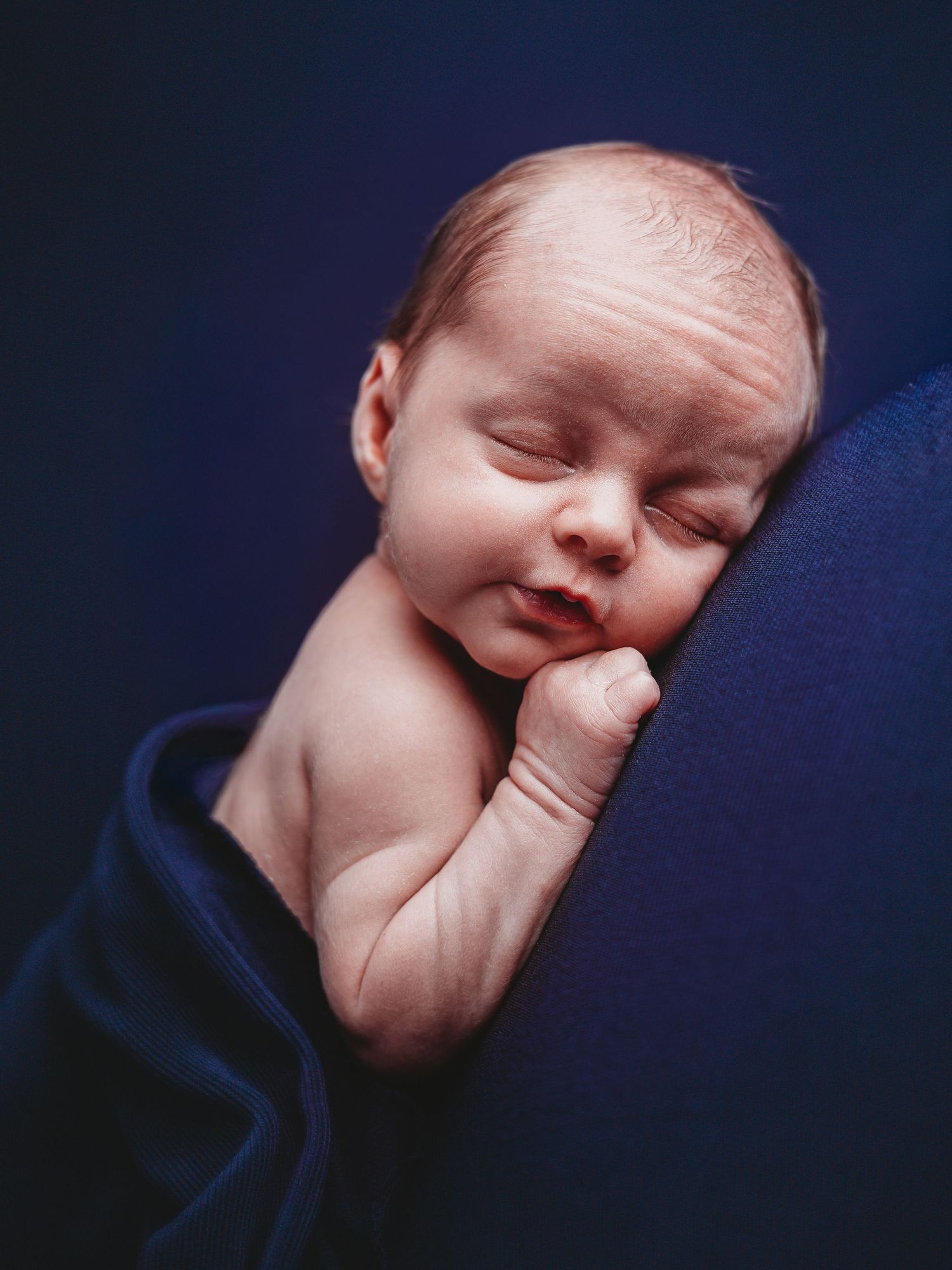 A sleeping newborn baby in profile view against a dark blue background.