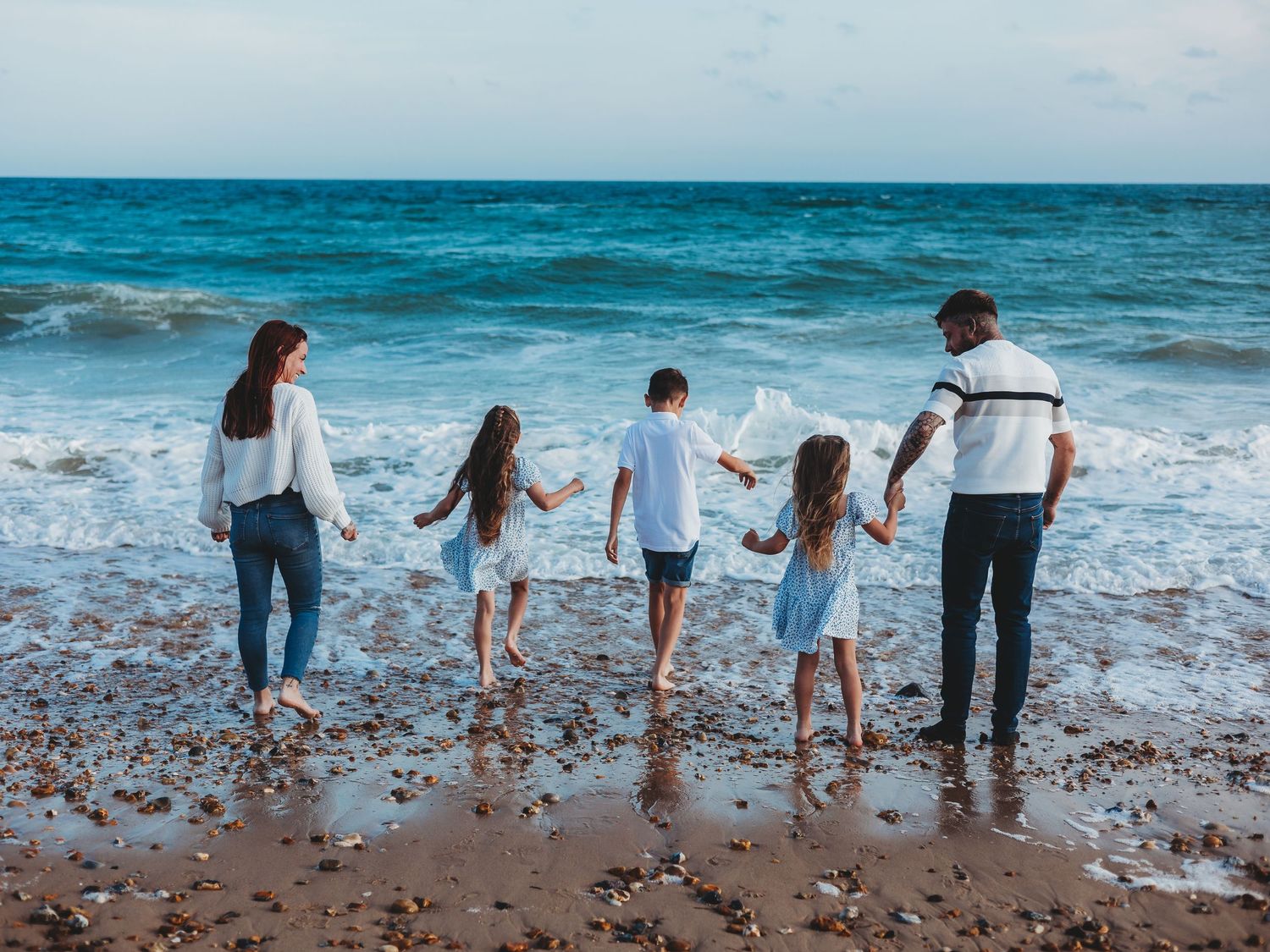 A group of people holding hands while walking along the shoreline of a beach with turquoise ocean waves.