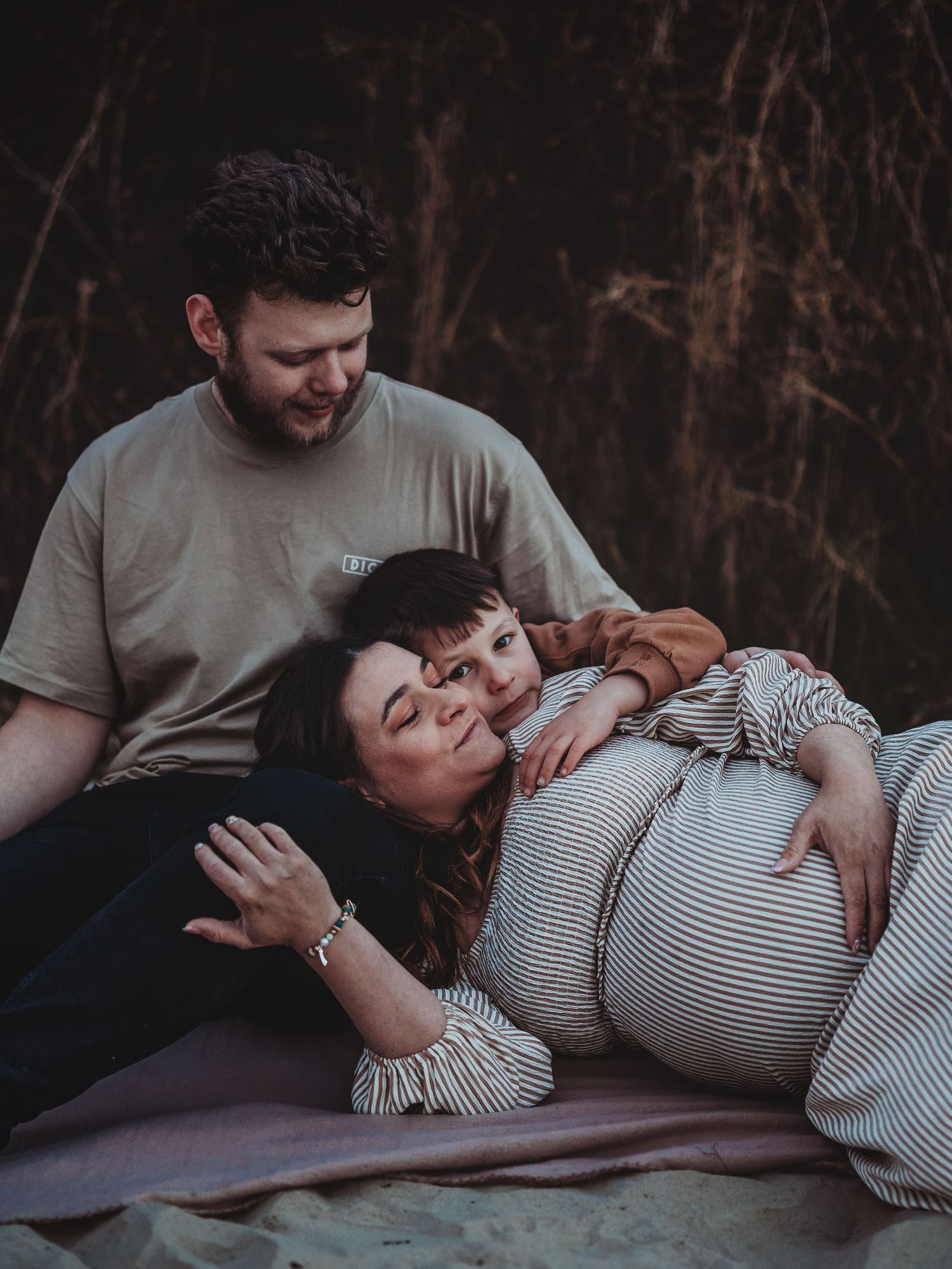 A family shares an intimate outdoor moment together while resting on a blanket at dusk.