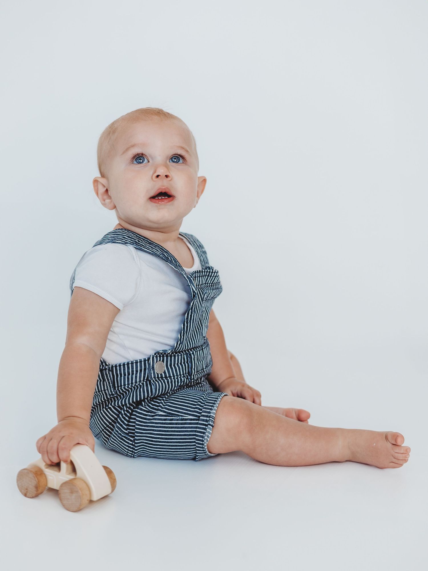 Baby in striped overalls sits on white background showing different poses and expressions.