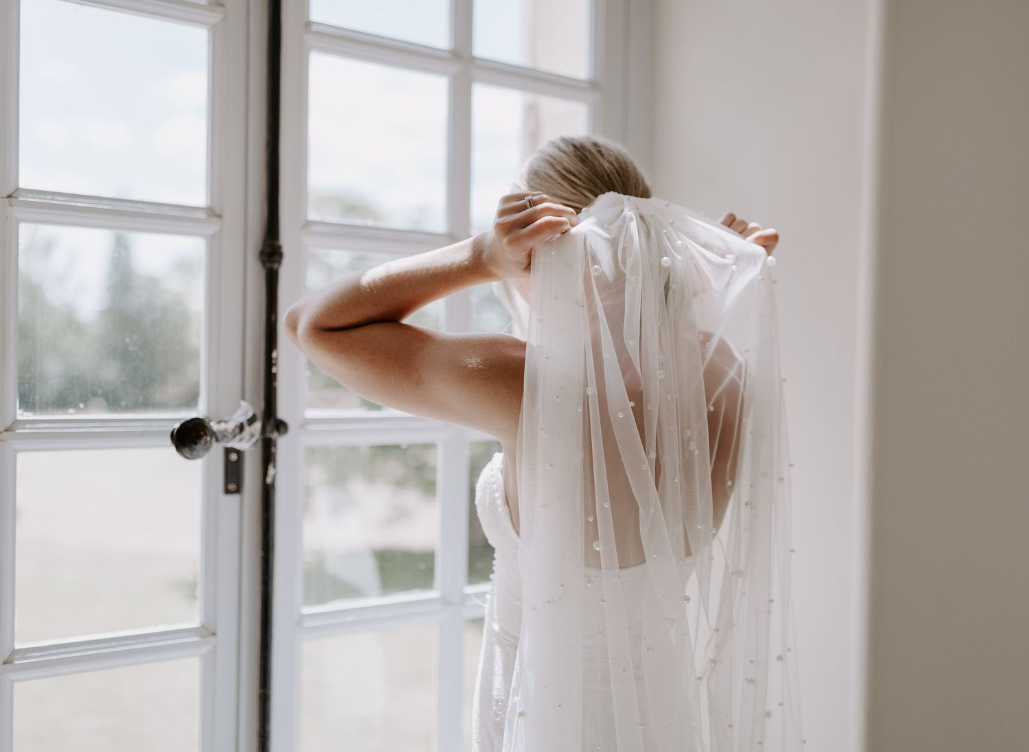 Wedding preparation scene with veil and natural window light in white room.