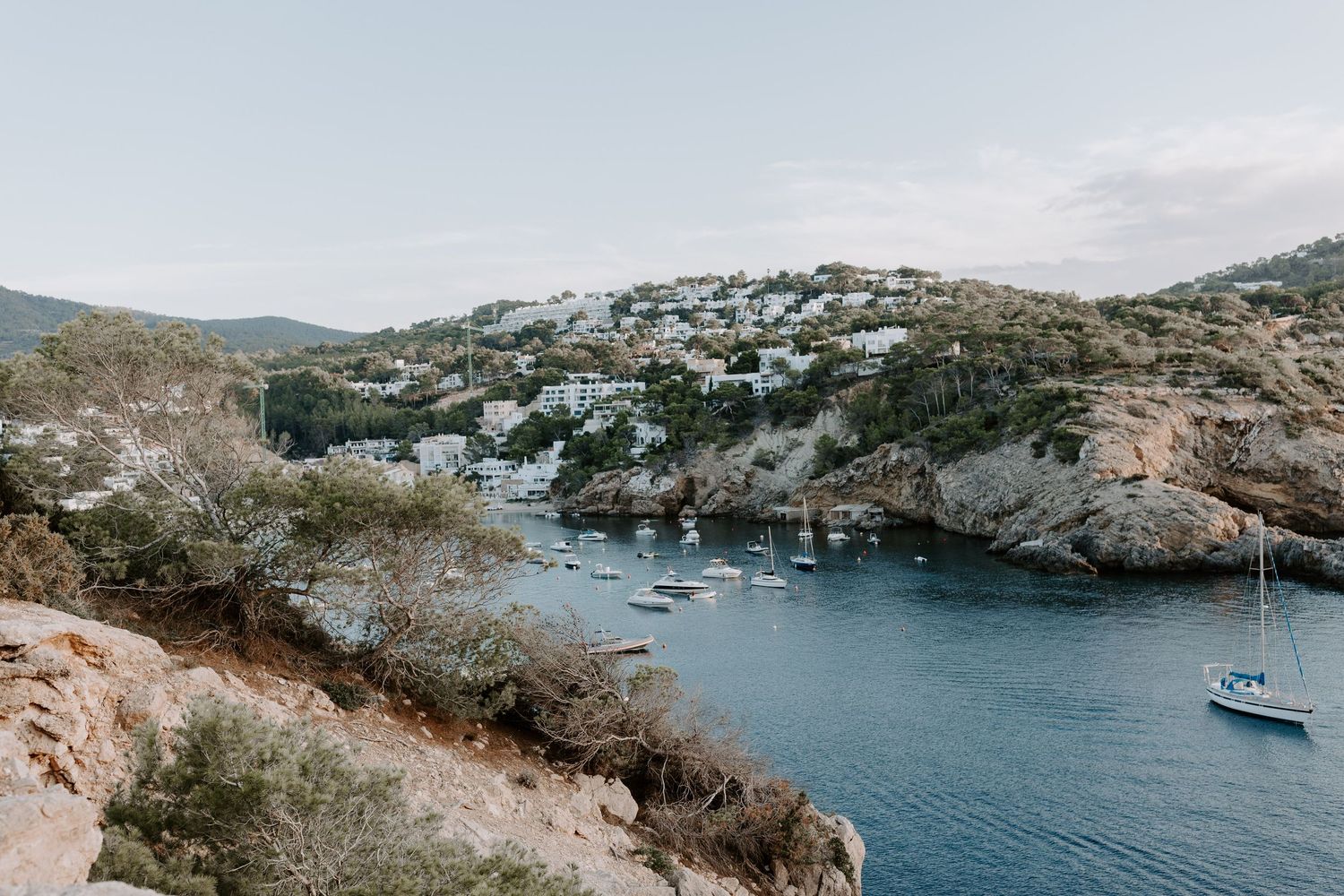 Scenic Menorca Mediterranean coastal view with rocky cliffs and boats anchored in a blue bay.