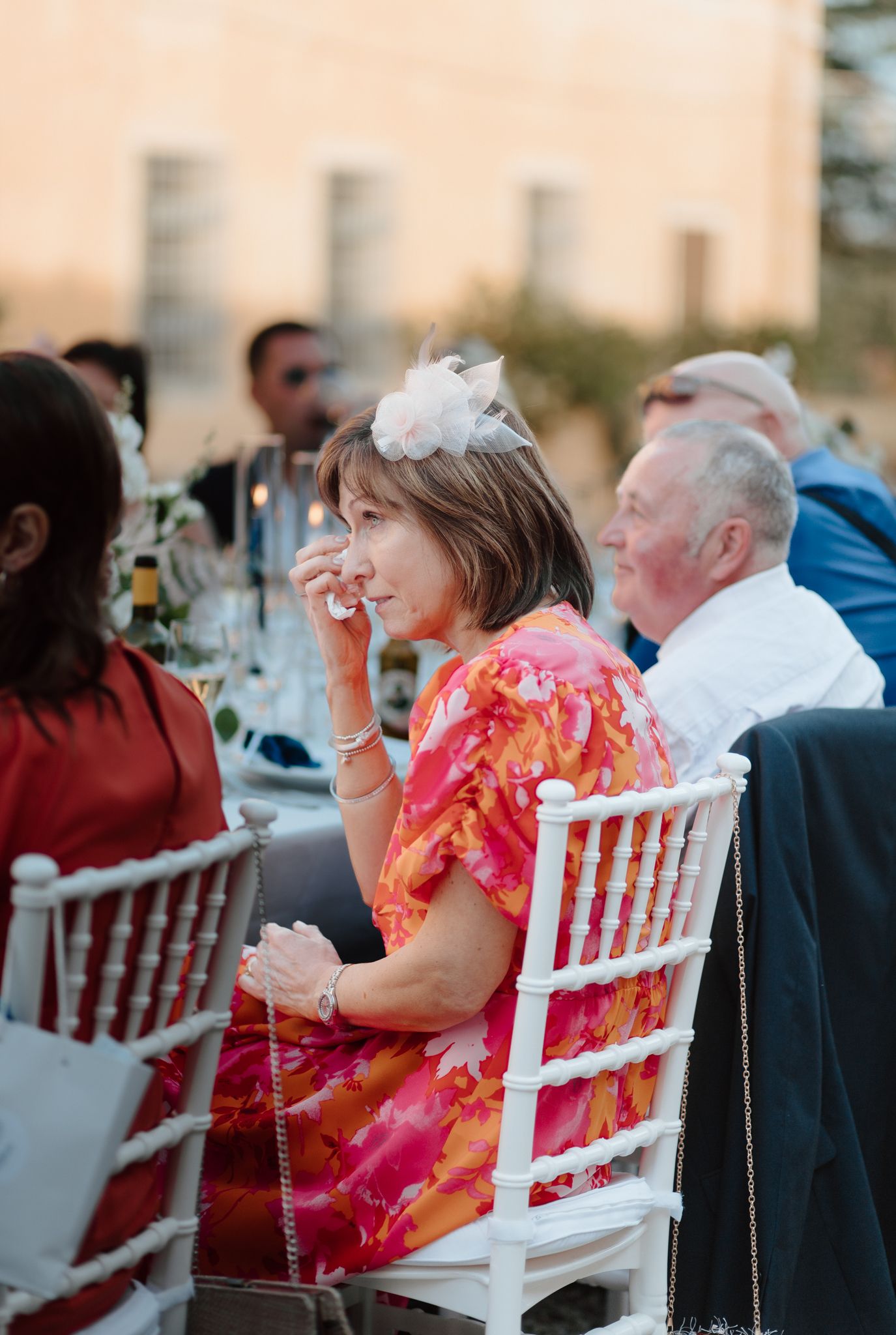 Wedding guests seated at outdoor dinner tables with white chairs.