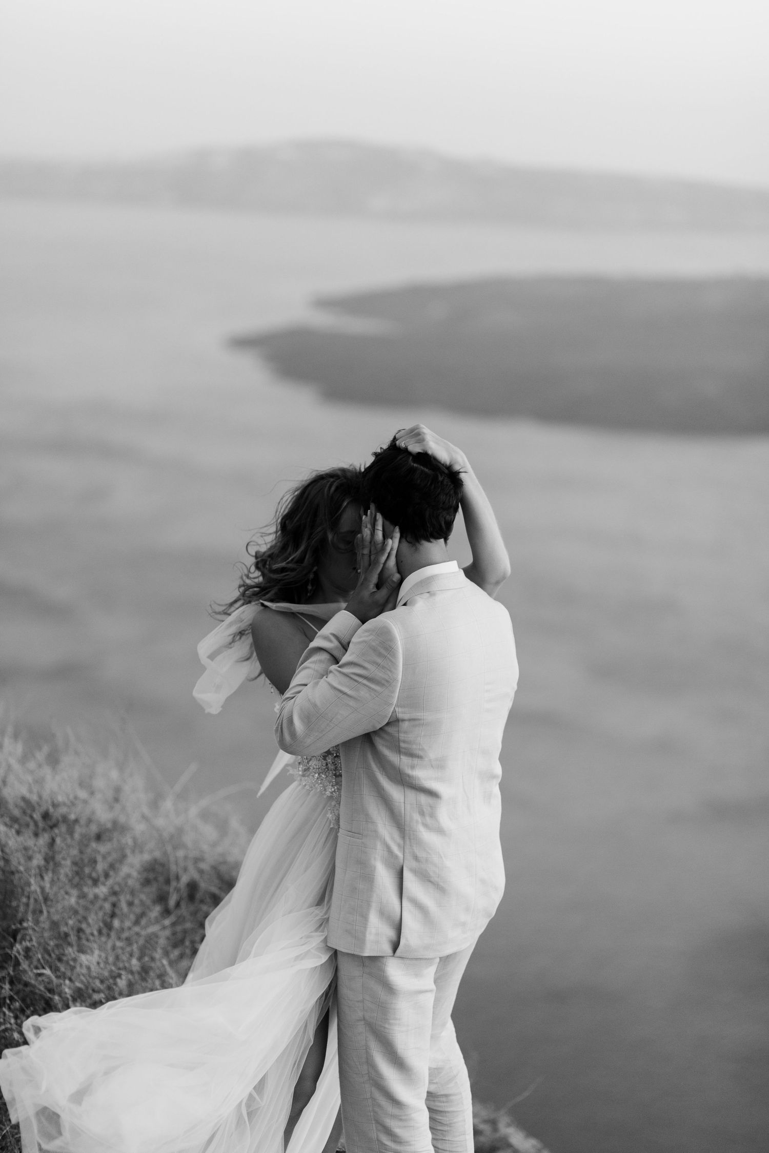 Dramatic black and white wedding photograph with flowing dress against coastal landscape in Santorini