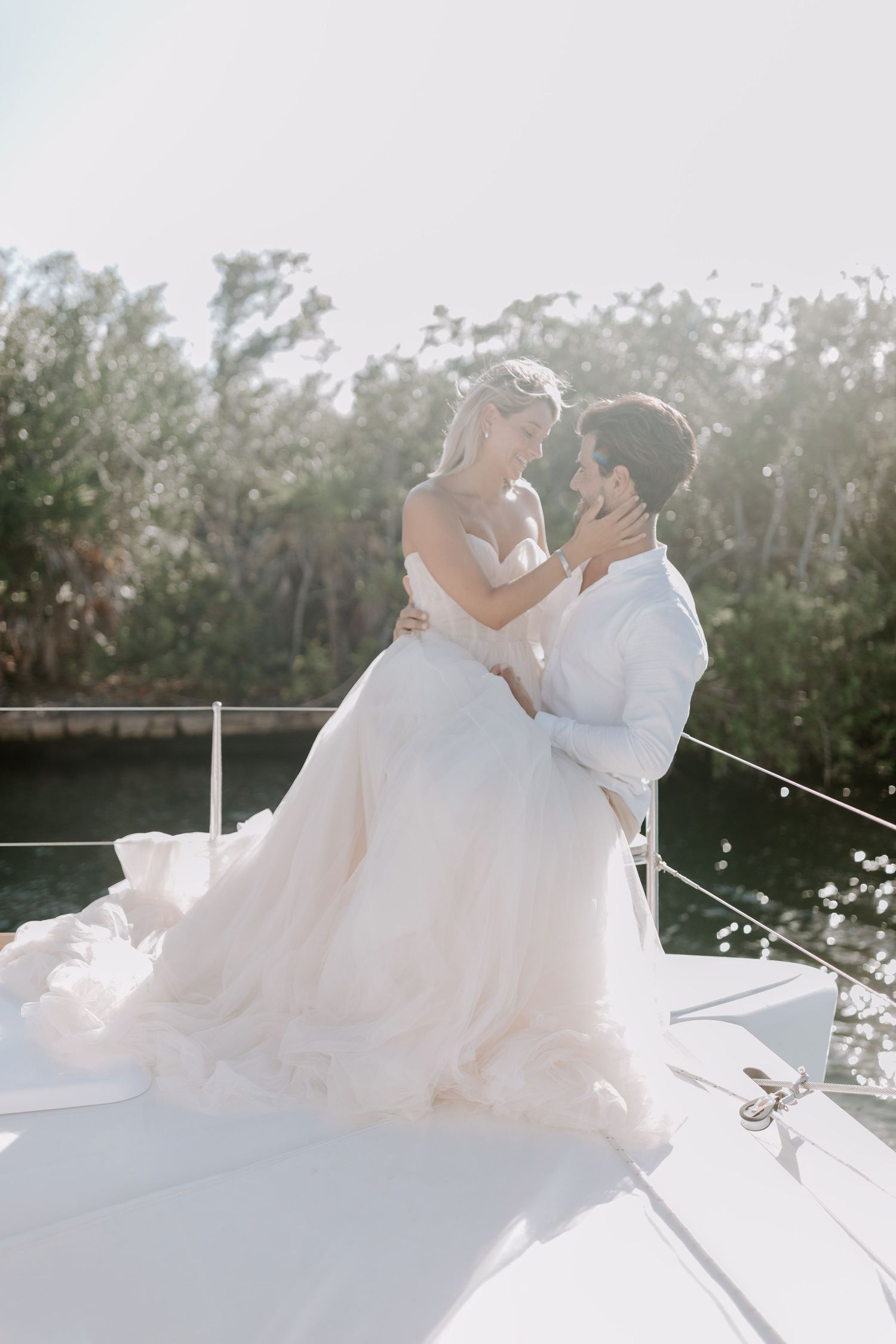 Couple in wedding attire sharing intimate moment on a sunny boat deck.
