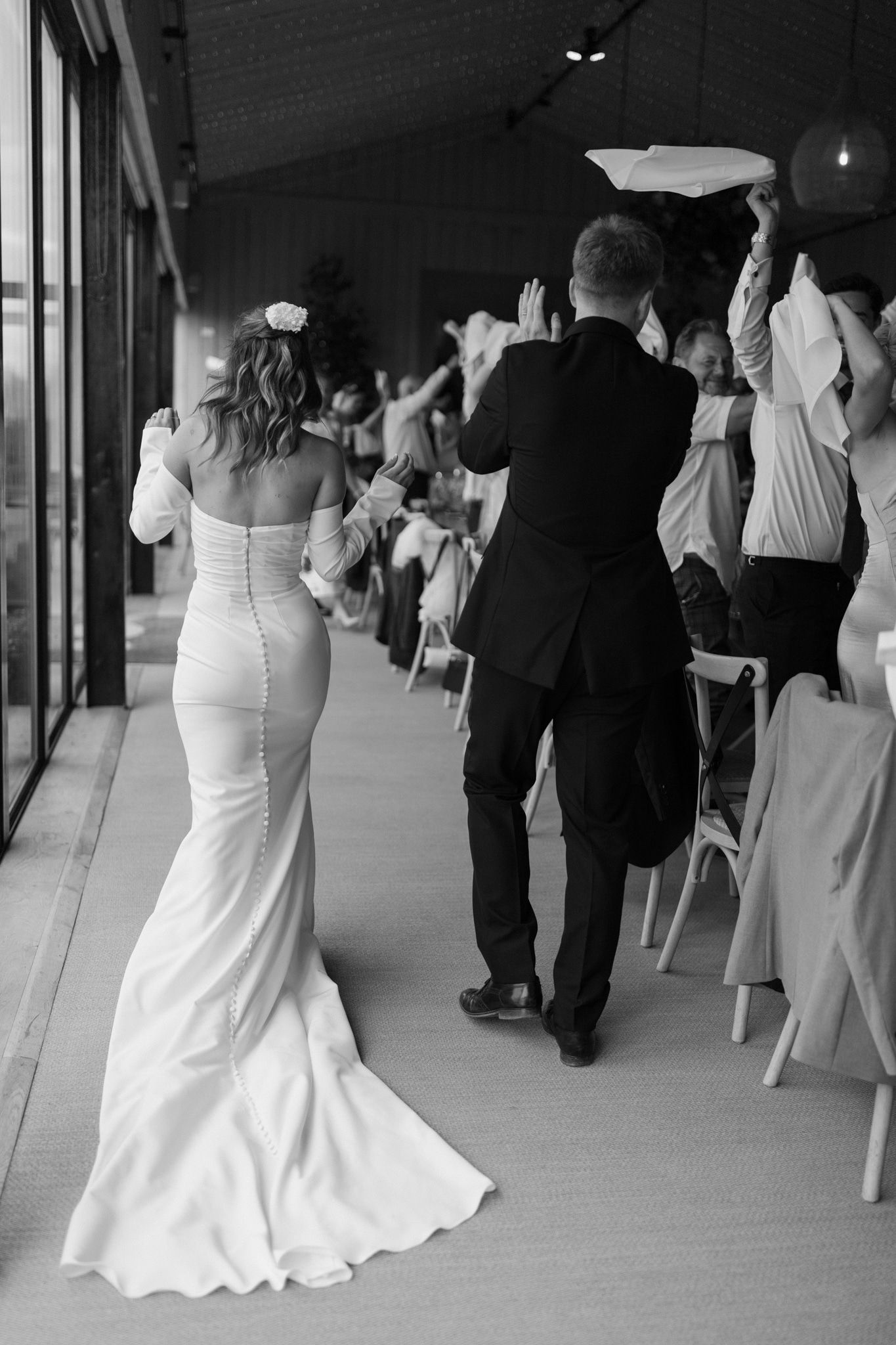 Wedding party walking in formal attire along a covered walkway in black and white.