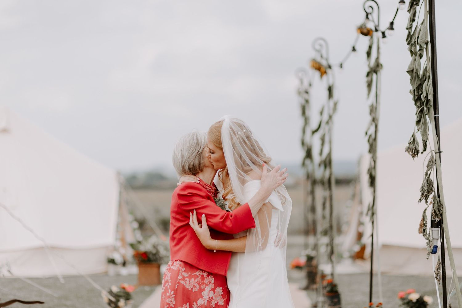 A couple in wedding attire embraces under hanging floral decorations.