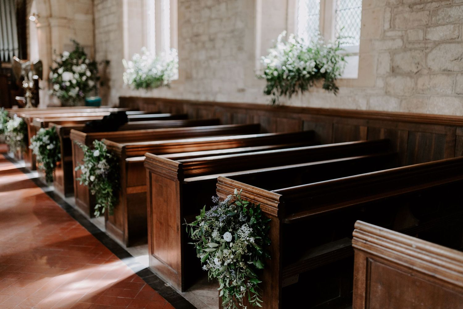 Church interior with wooden pews decorated with floral arrangements for a wedding ceremony.
