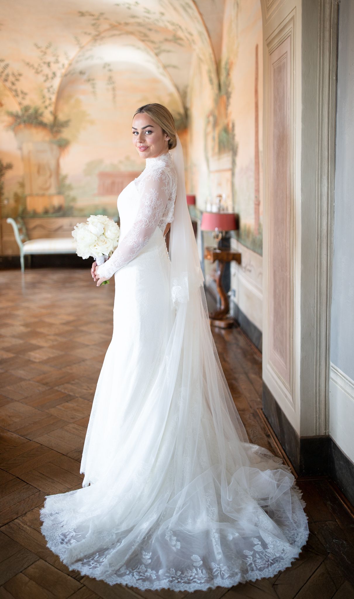 Elegant wedding gown with lace details and flowing train in ornate indoor setting.
