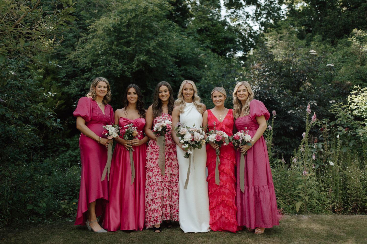Wedding party in pink dresses posing together in an outdoor garden setting.