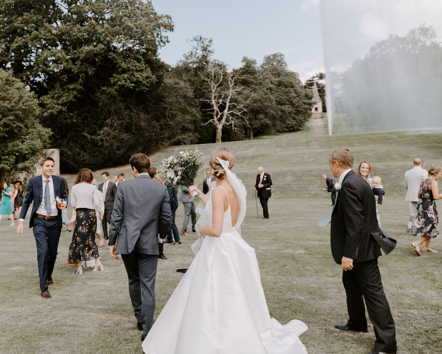 Outdoor wedding celebration on a grassy hillside with guests gathered around.
