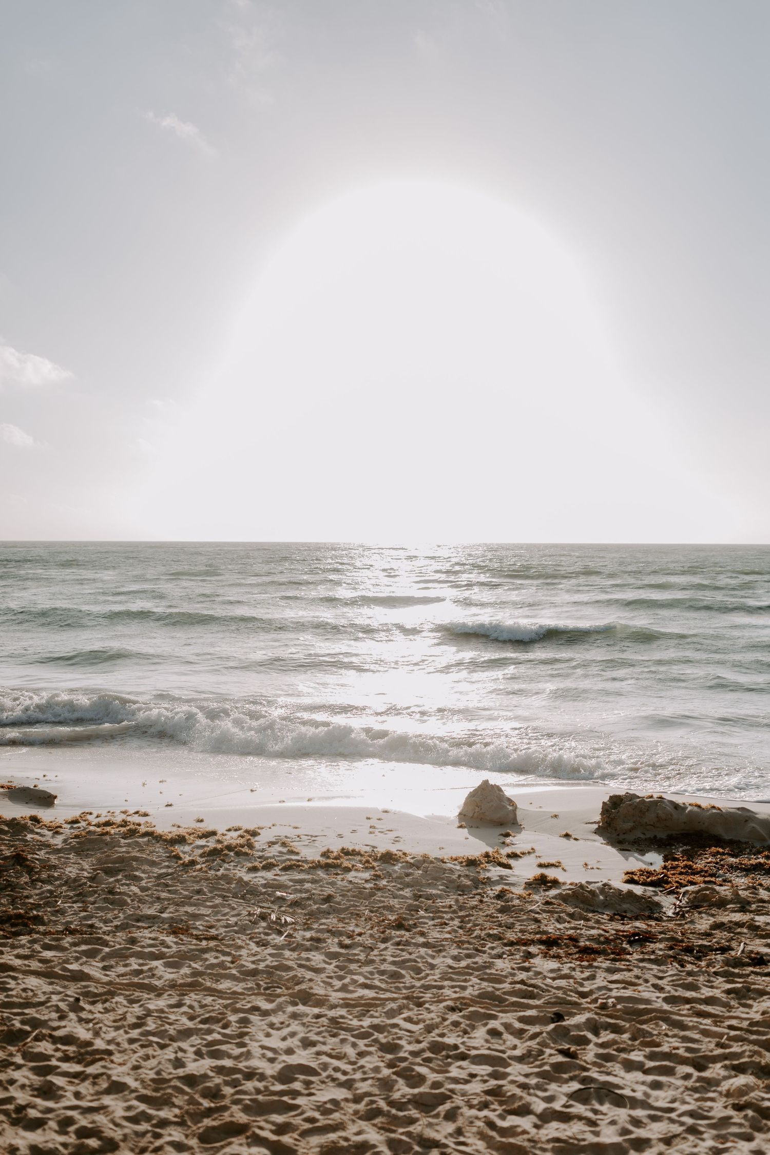 Scenic beach landscape with rocky shoreline and waves under bright sunlight.