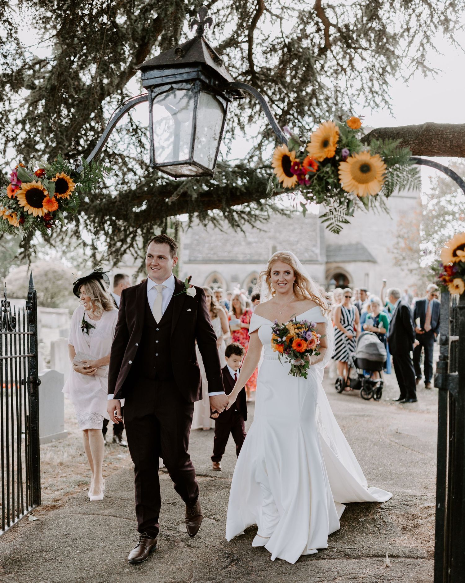 Wedding procession walking through garden gates with bright sunflower bouquets.