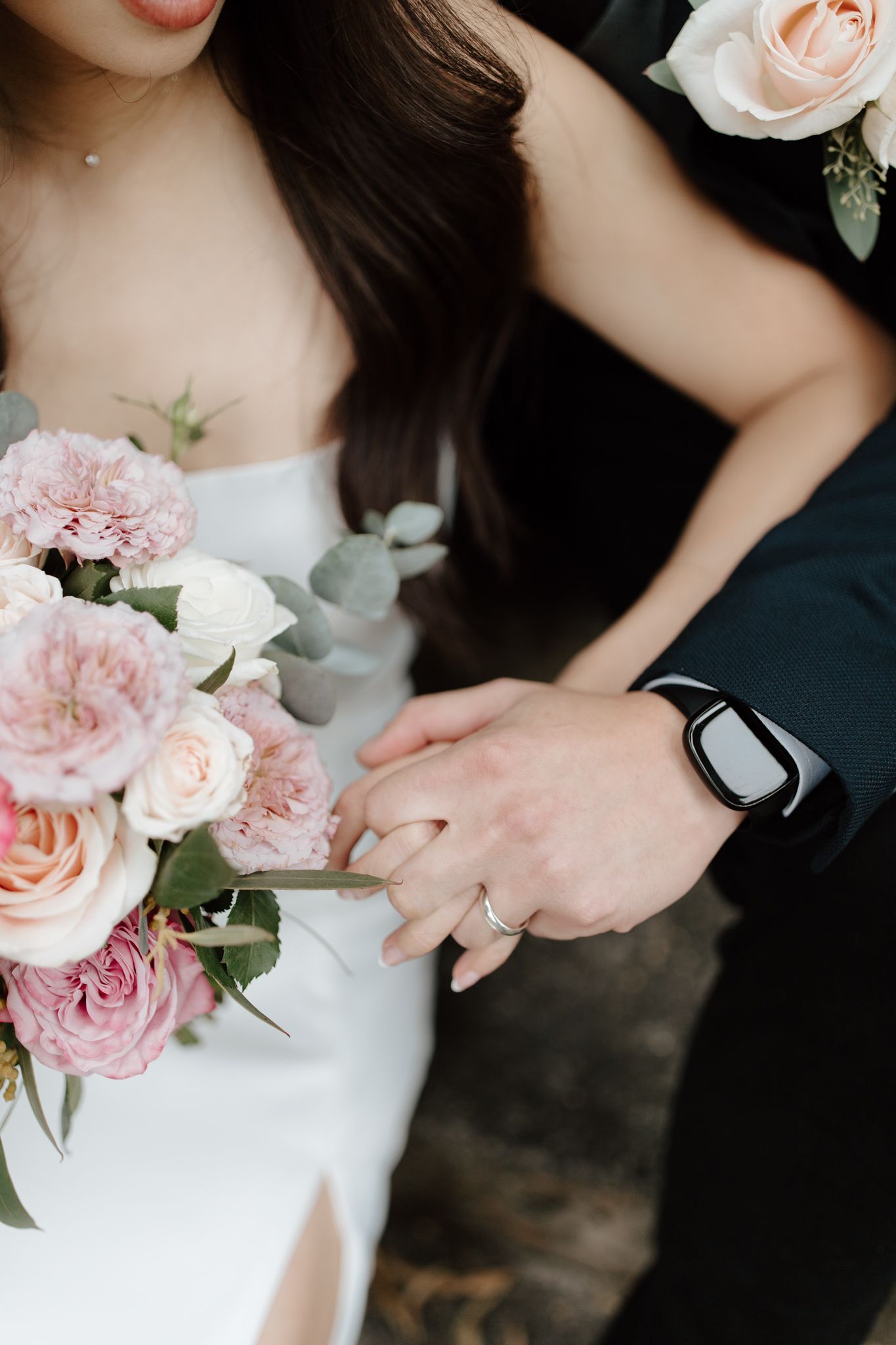 Close-up of wedding bouquet with pink roses and hands showing wedding rings.