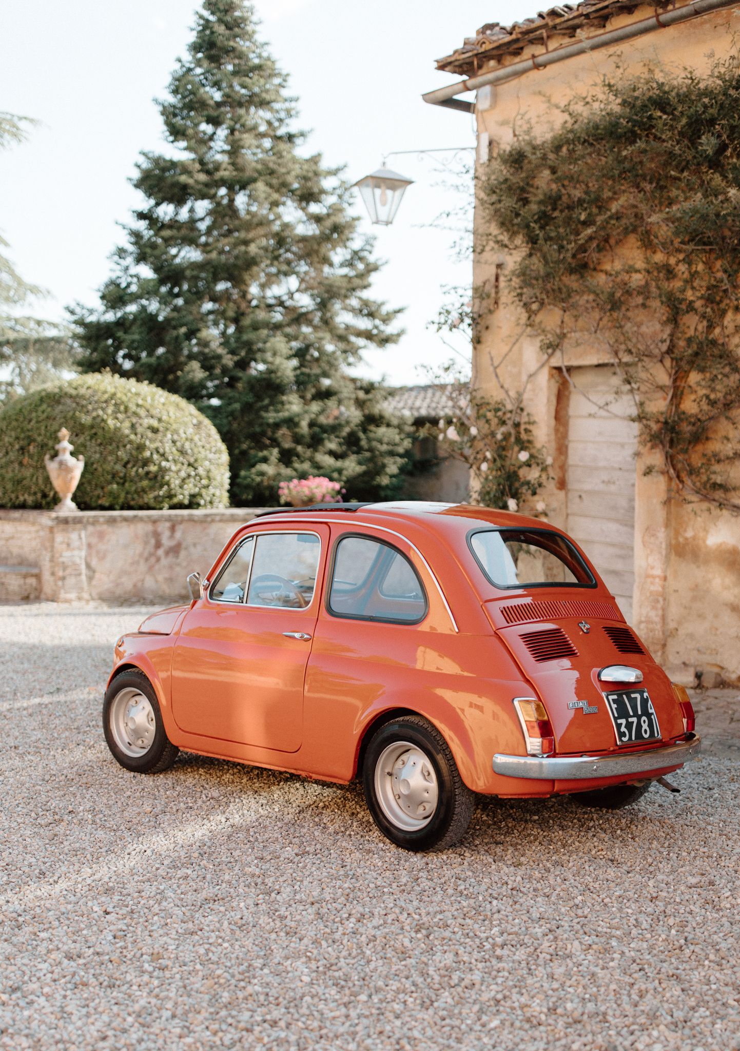 Vintage orange Fiat 500 parked outside rustic Italian villa.