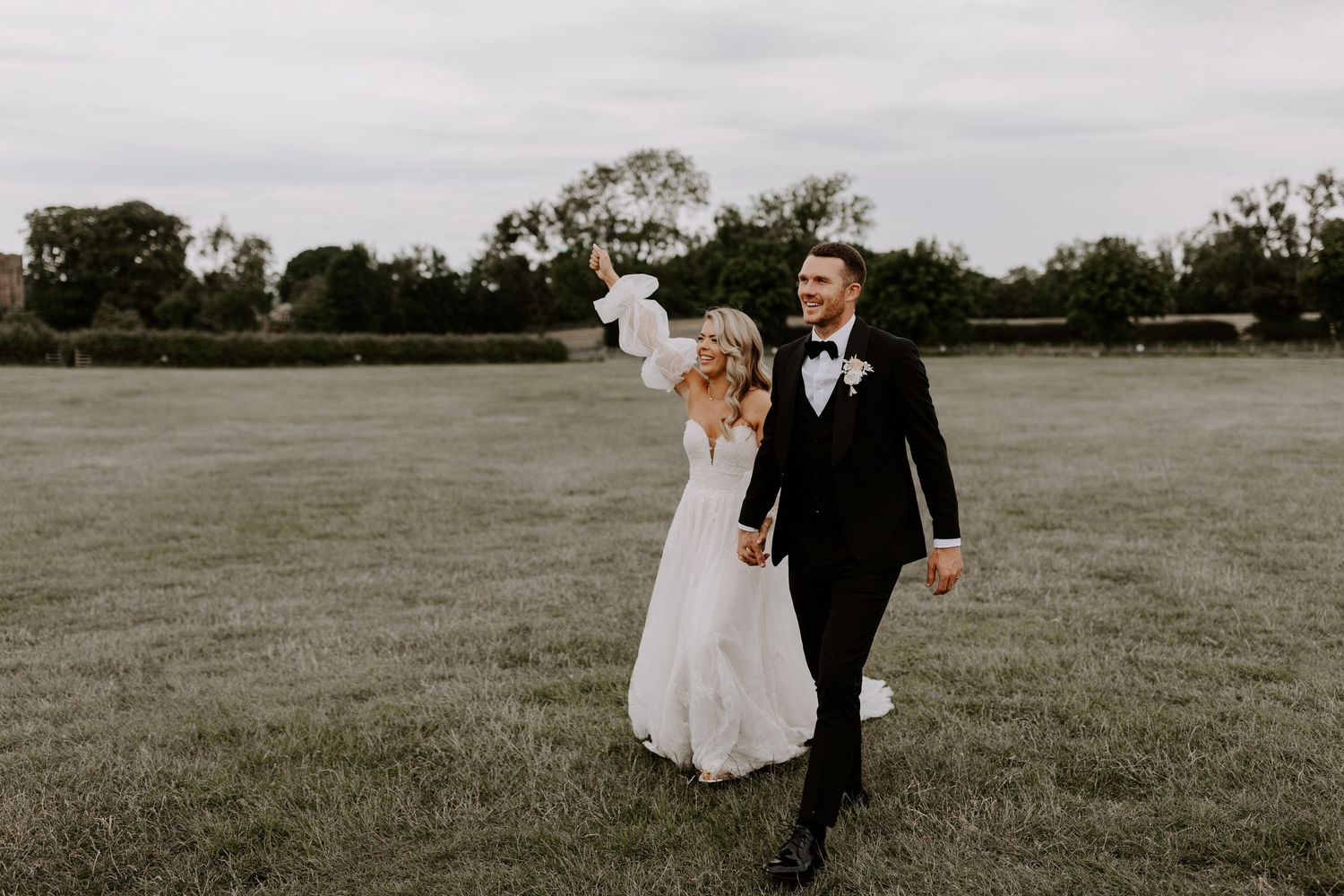 Happy couple walking hand in hand across a vast green field.