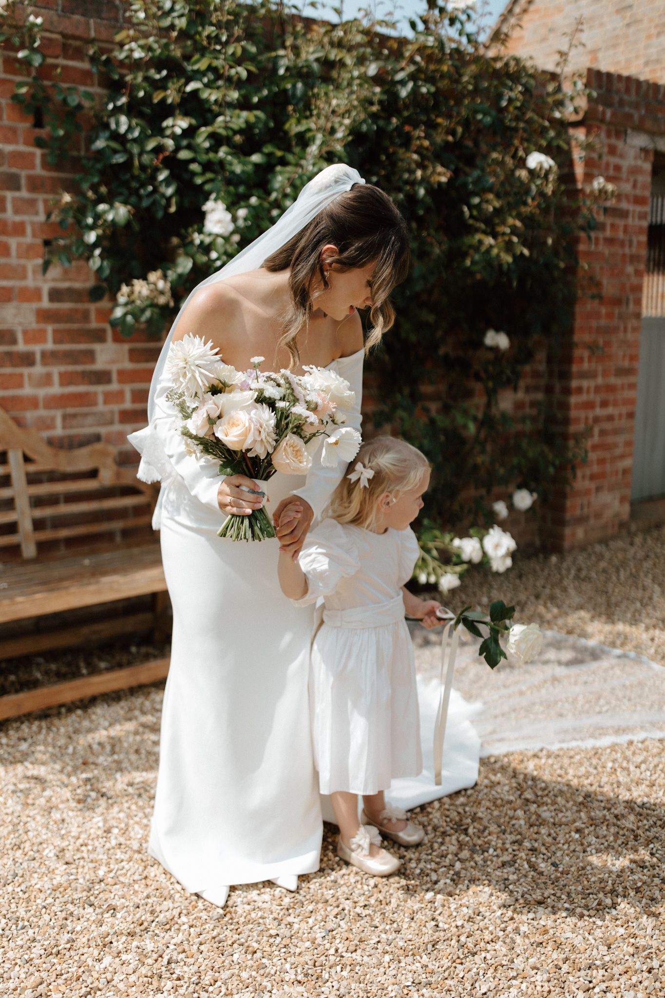 A tender moment between a parent and child in white dresses against a brick wall backdrop.