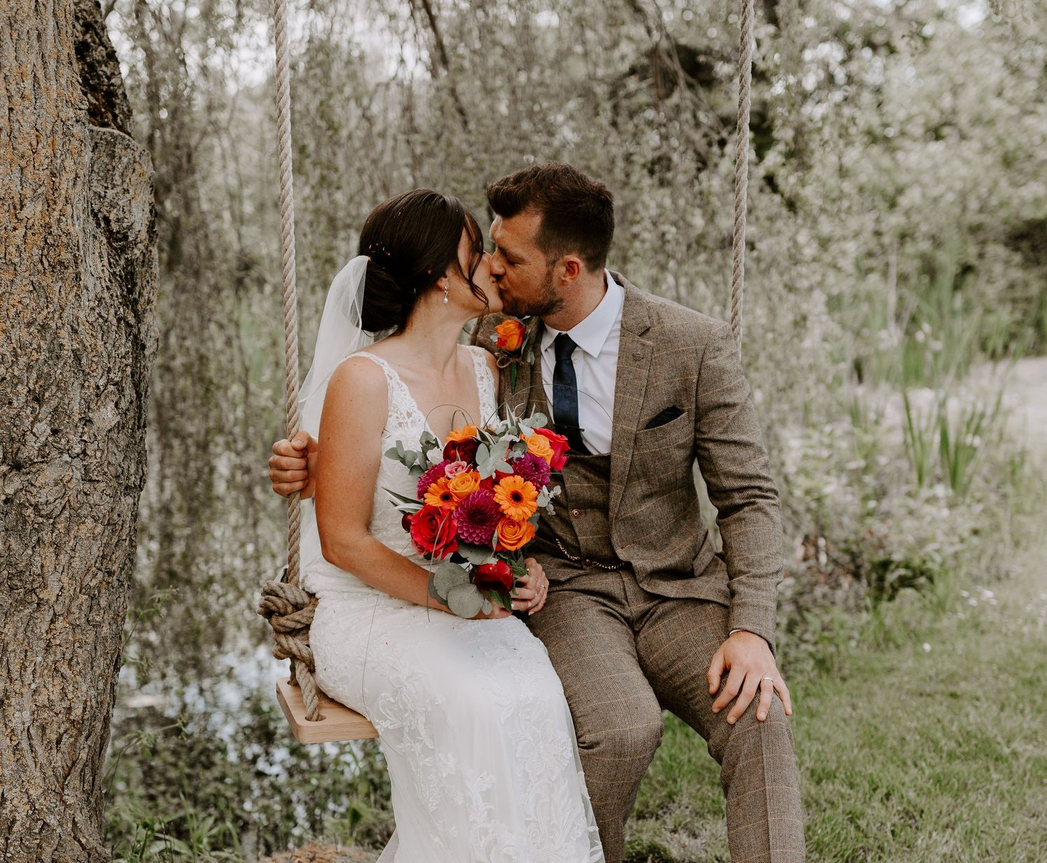 Wedding couple in rustic woodland setting with vibrant autumn bouquet.