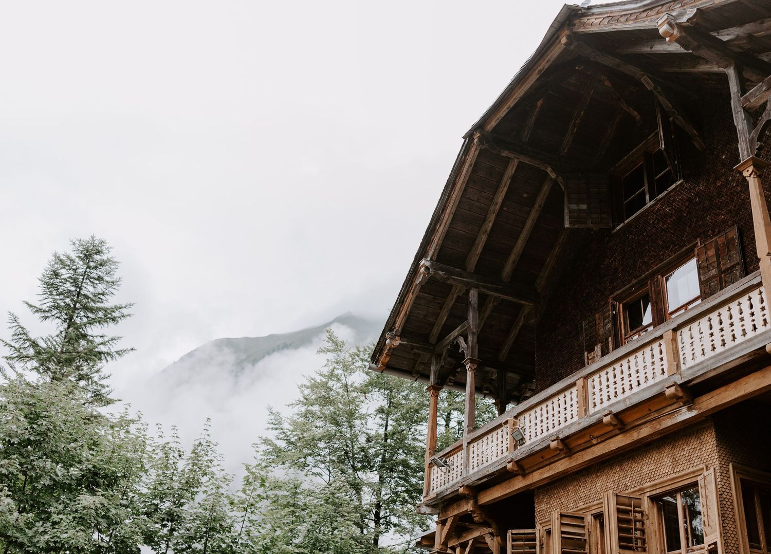 Rustic wooden chalet with mountain peaks visible in misty background.