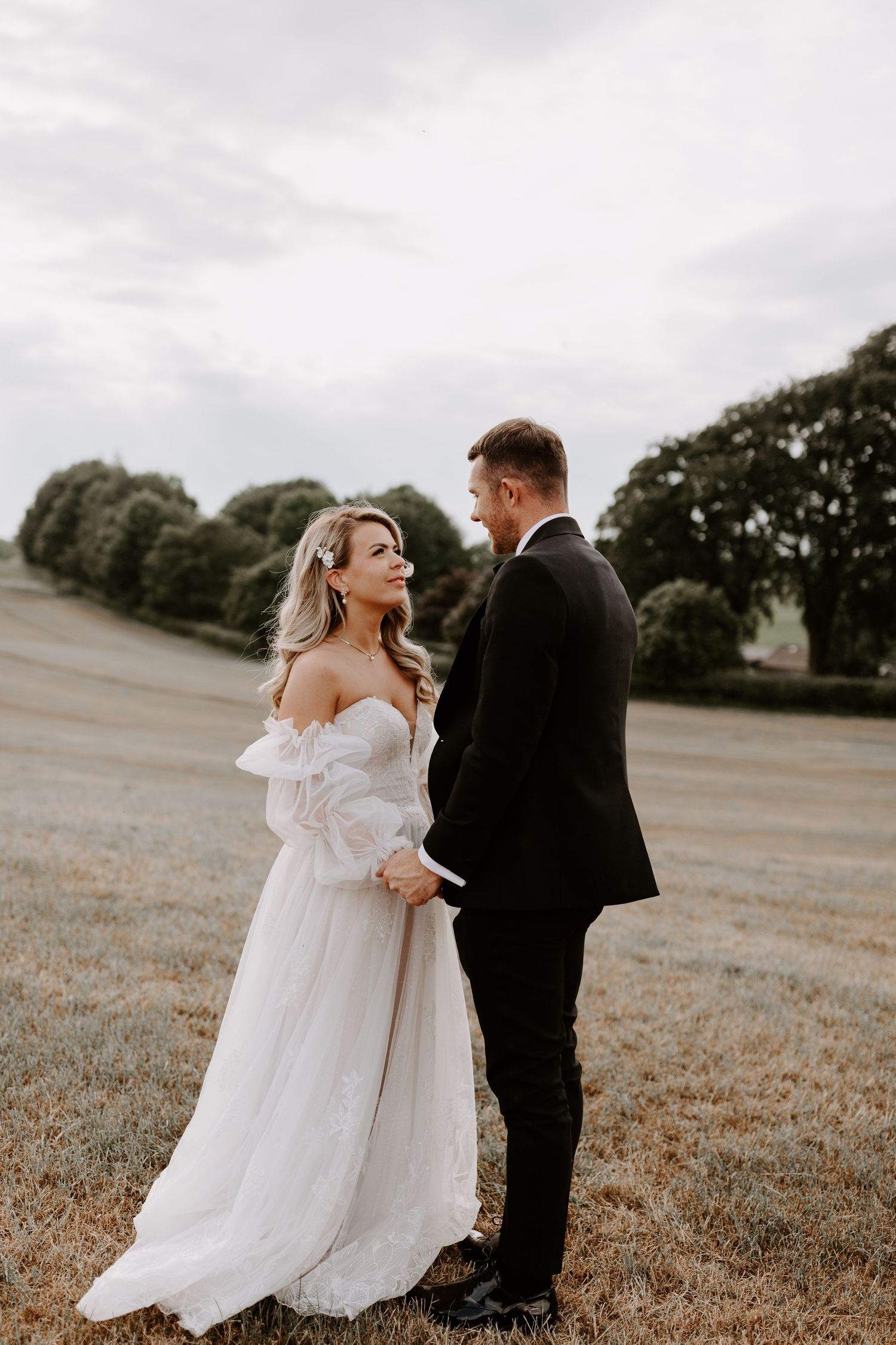 Couple in wedding attire sharing an intimate moment in a sunlit field.