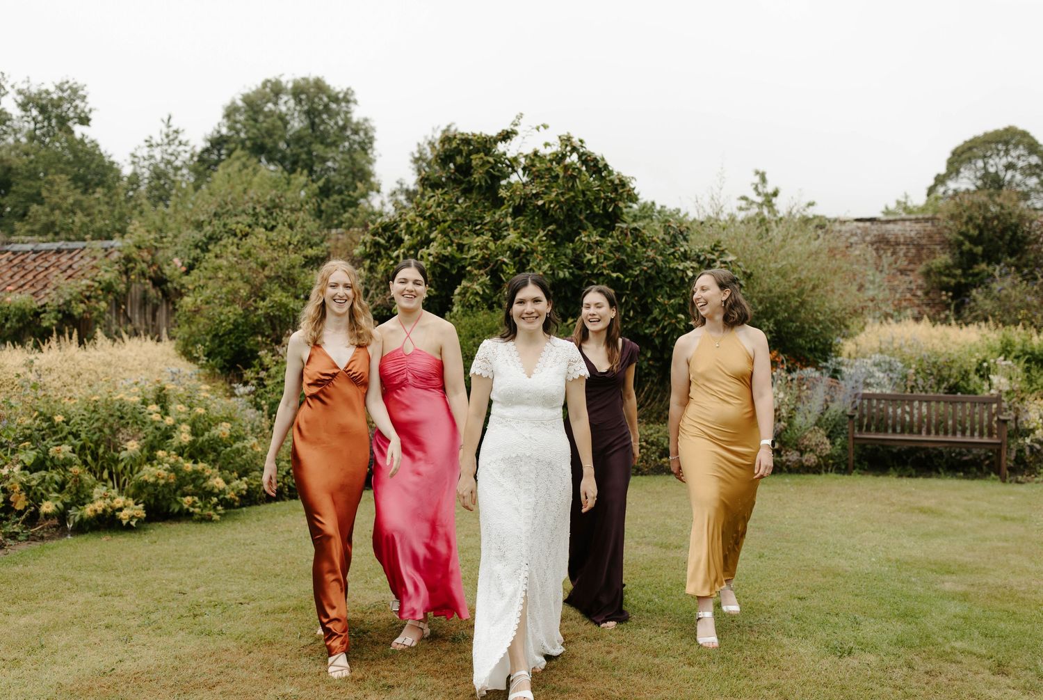 Wedding group walking through a garden setting in pink and neutral colored dresses.