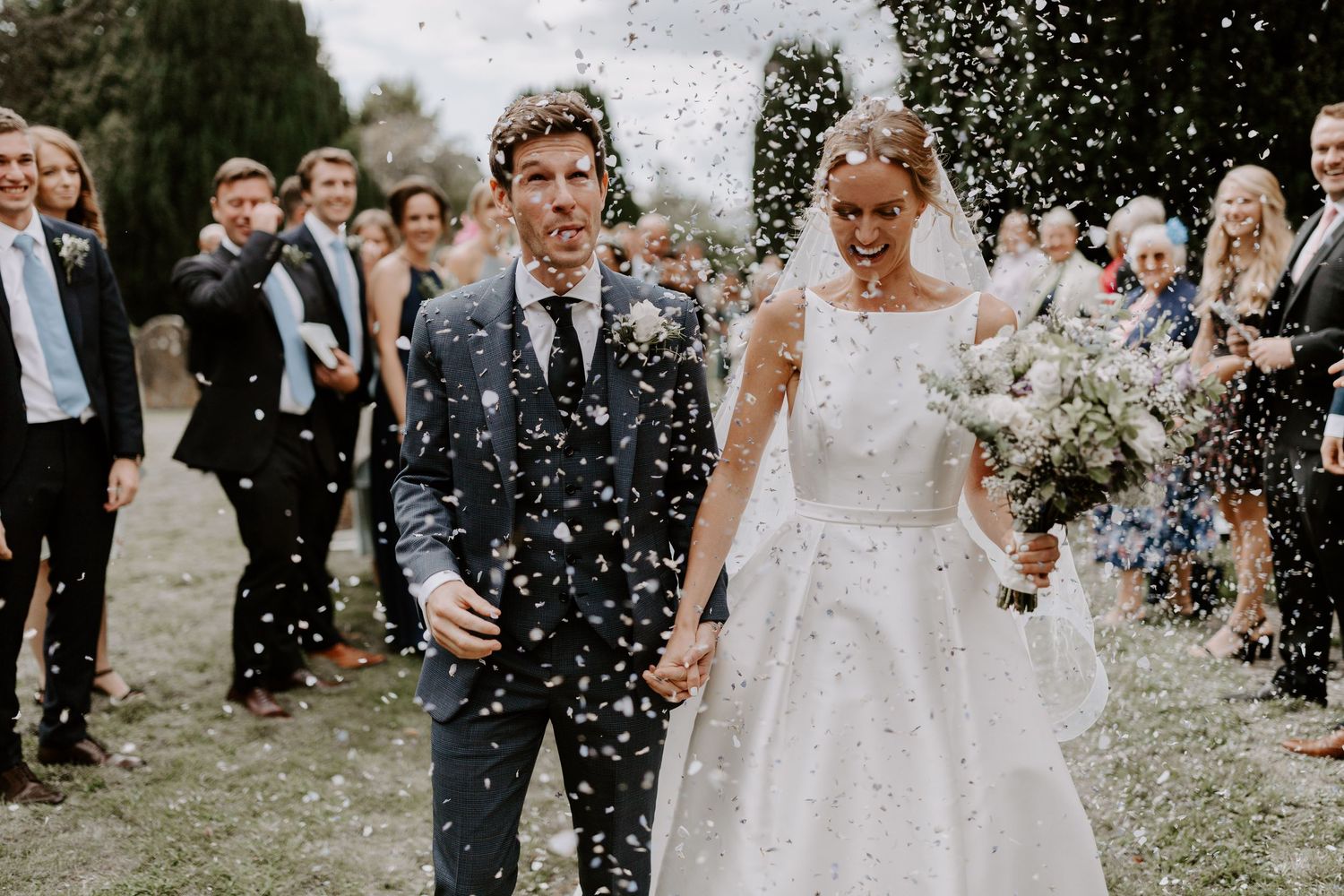 Wedding celebration with guests throwing confetti in an outdoor garden setting.