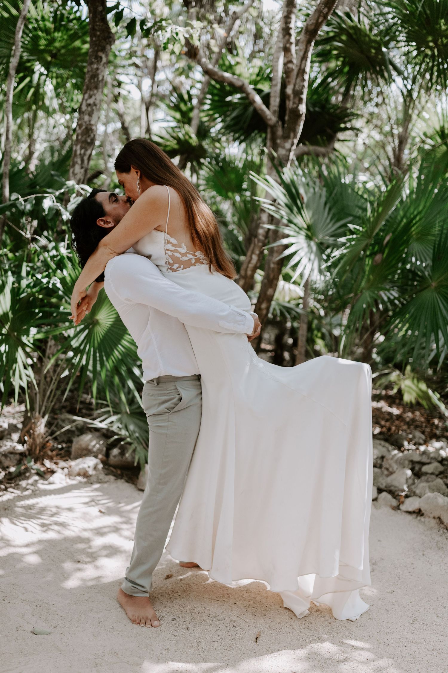 A couple embraces in a tropical garden setting with palm trees and natural sunlight.