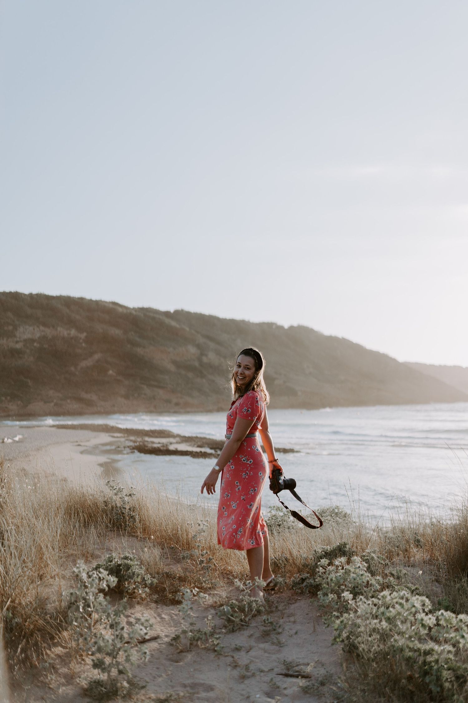 Coastal portrait with someone in a red floral dress against an ocean backdrop at sunset.