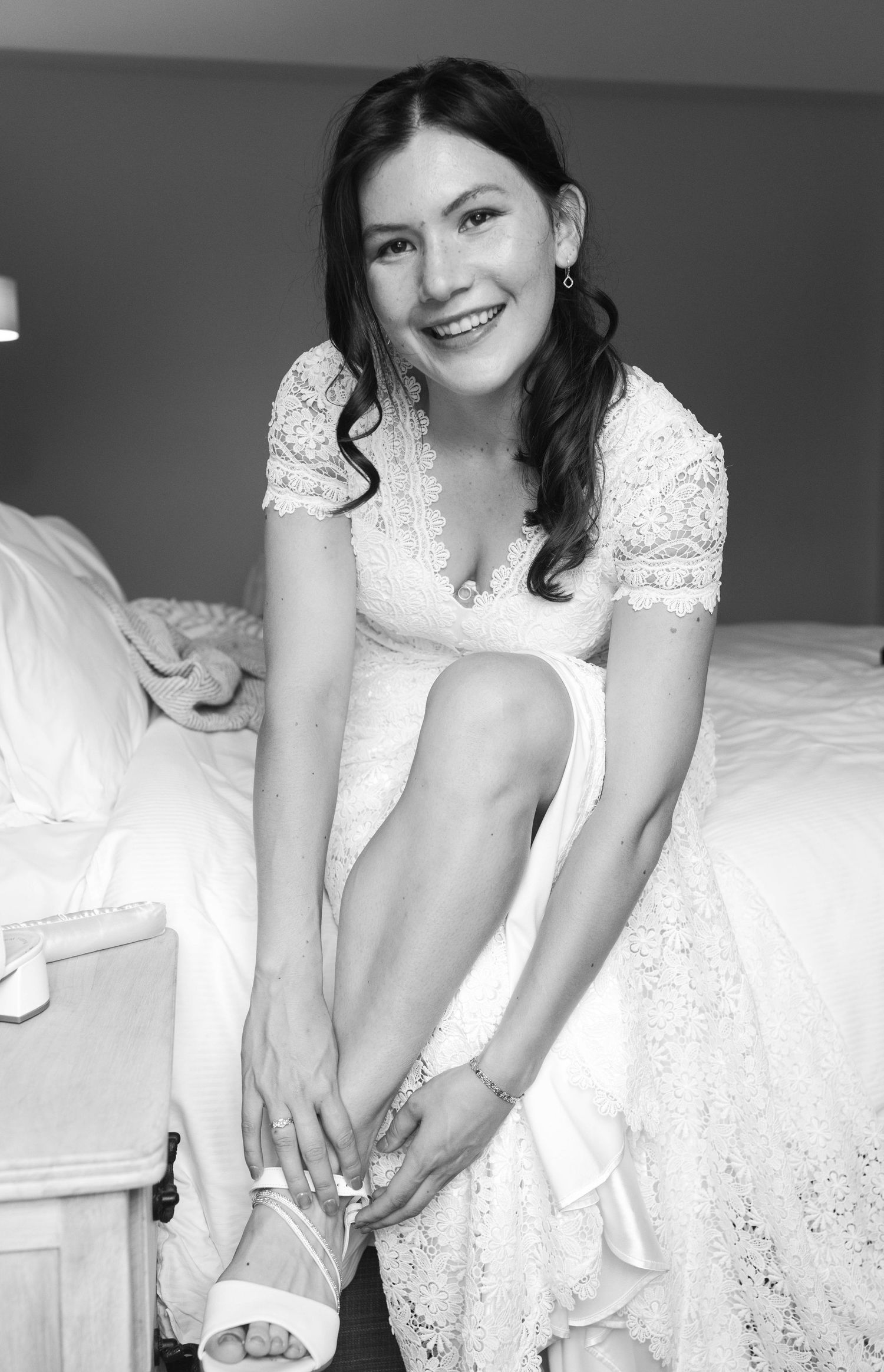Bride in a white lace wedding dress adjusting their shoes while getting ready