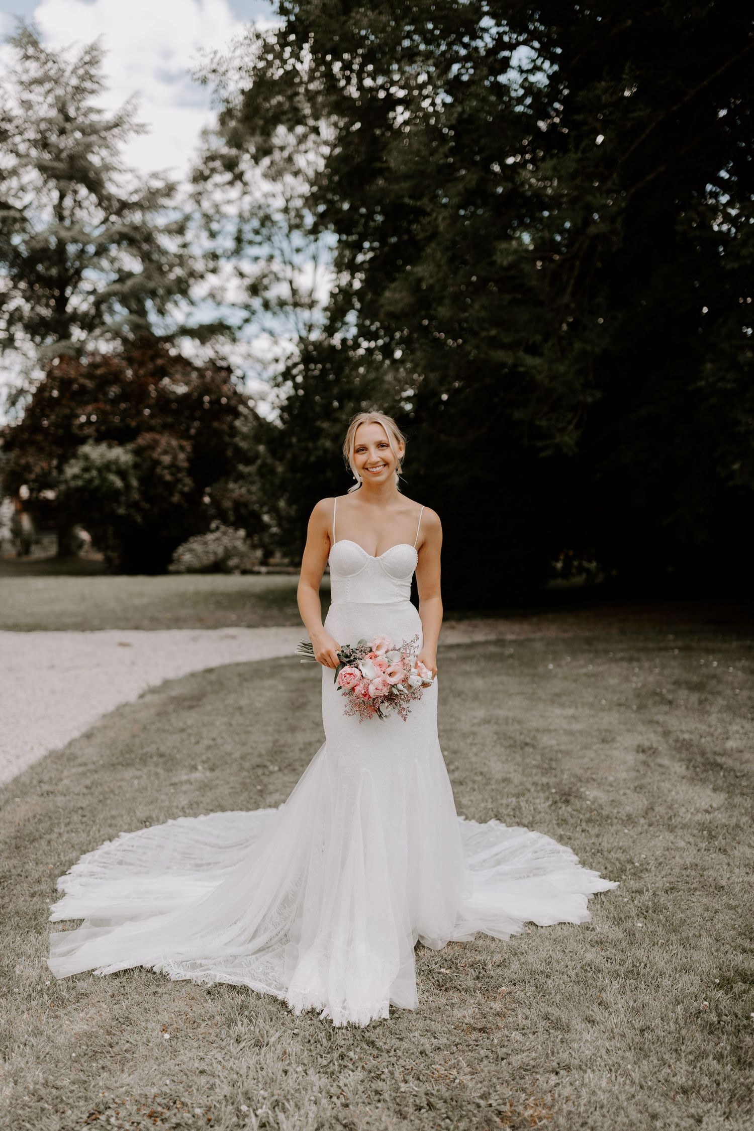 Bride in a classic white gown sits gracefully on grassy terrain holding a floral bouquet.