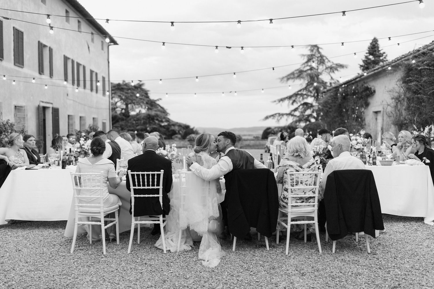Outdoor wedding reception with string lights and white chairs on villa terrace.