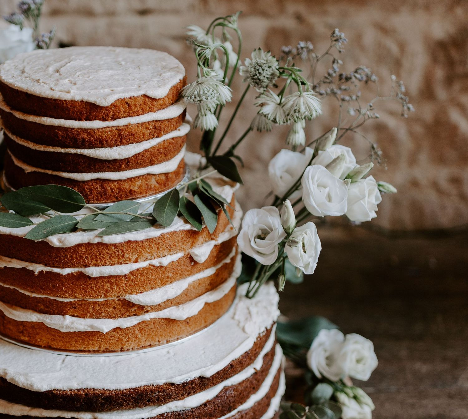 Rustic naked wedding cake decorated with white flowers and cream frosting between layers.