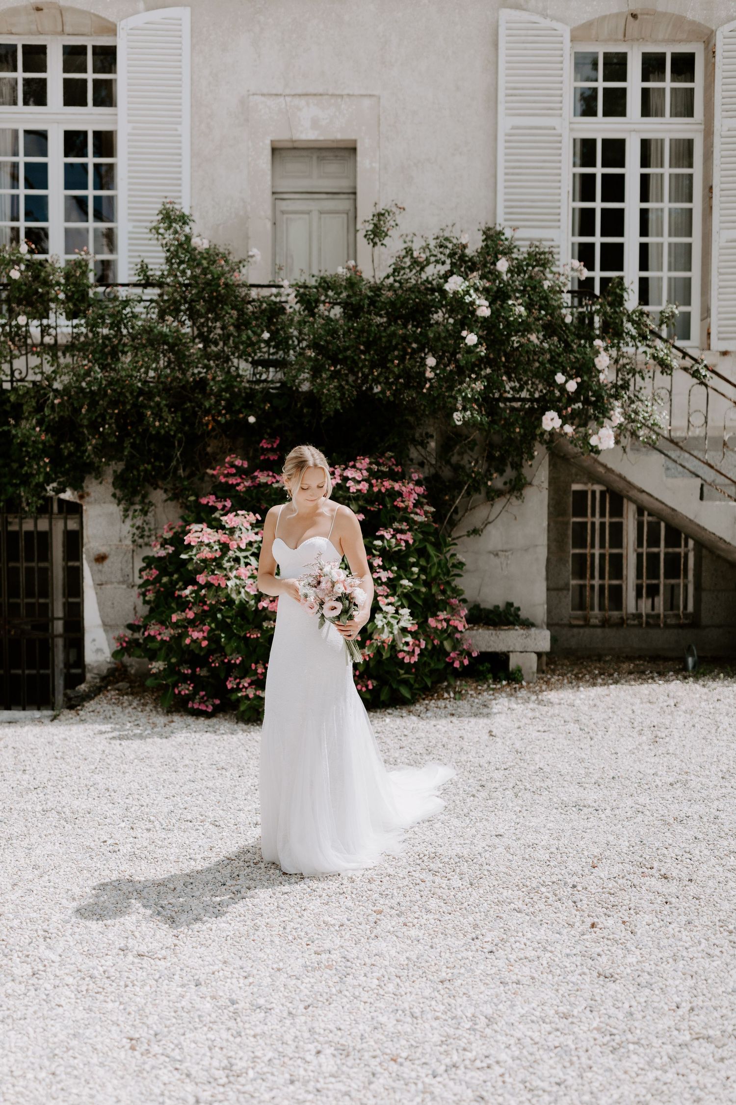 Wedding dress portrait against a white mansion exterior with blooming rose bushes.