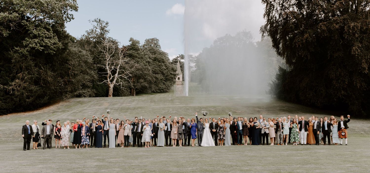 Large wedding group photo with guests lined up on a grassy field.
