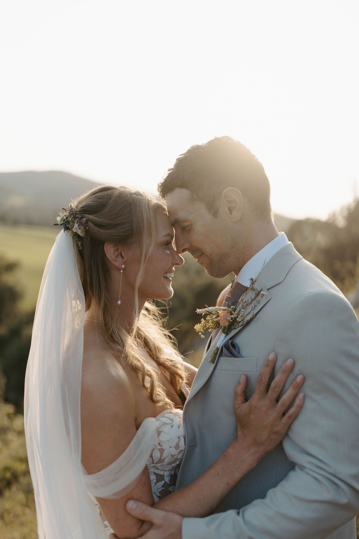 A couple in wedding attire shares an intimate moment in golden sunlight.
