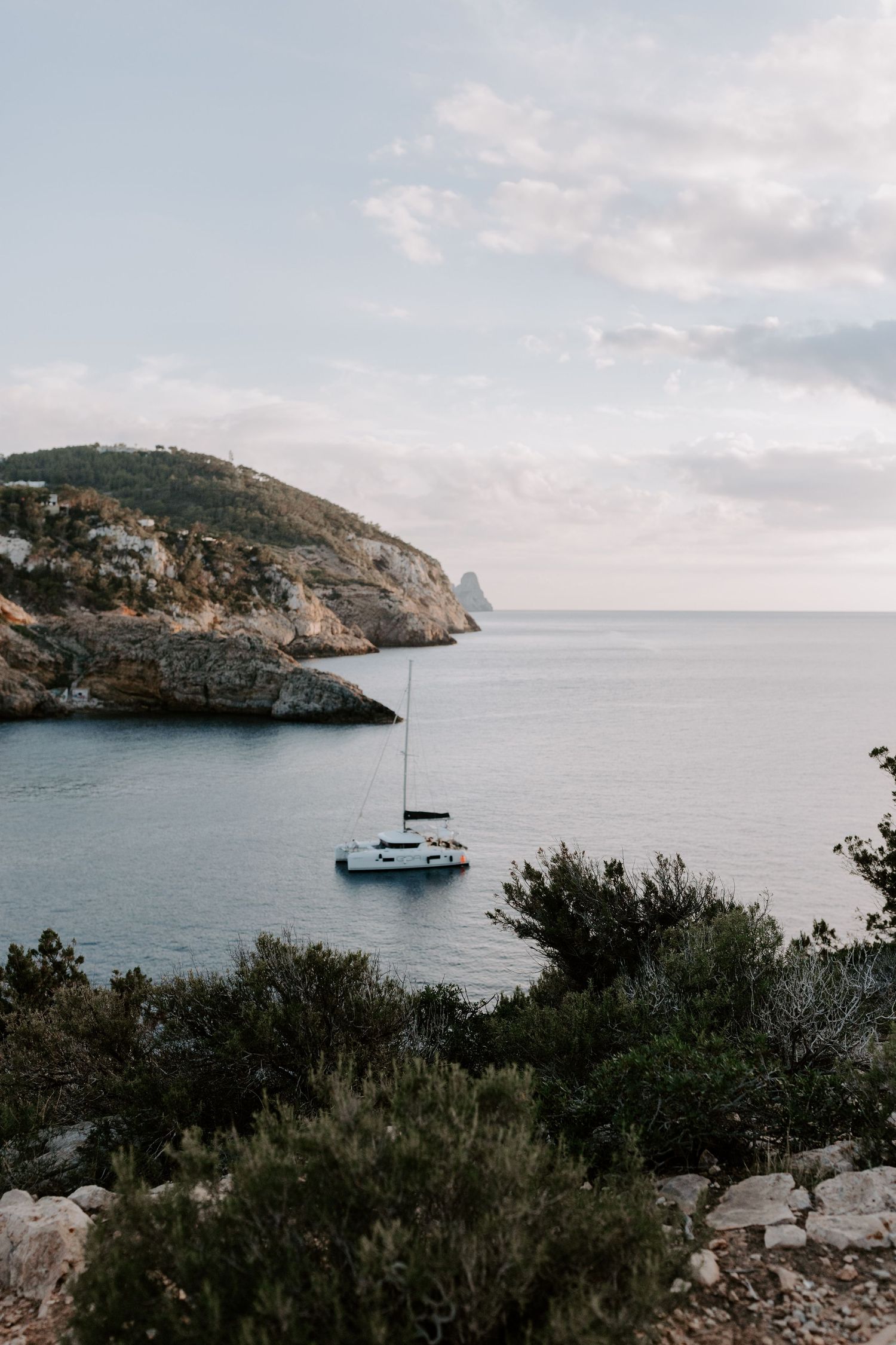 Sailboat anchored in serene Mediterranean cove with rocky cliffs.
