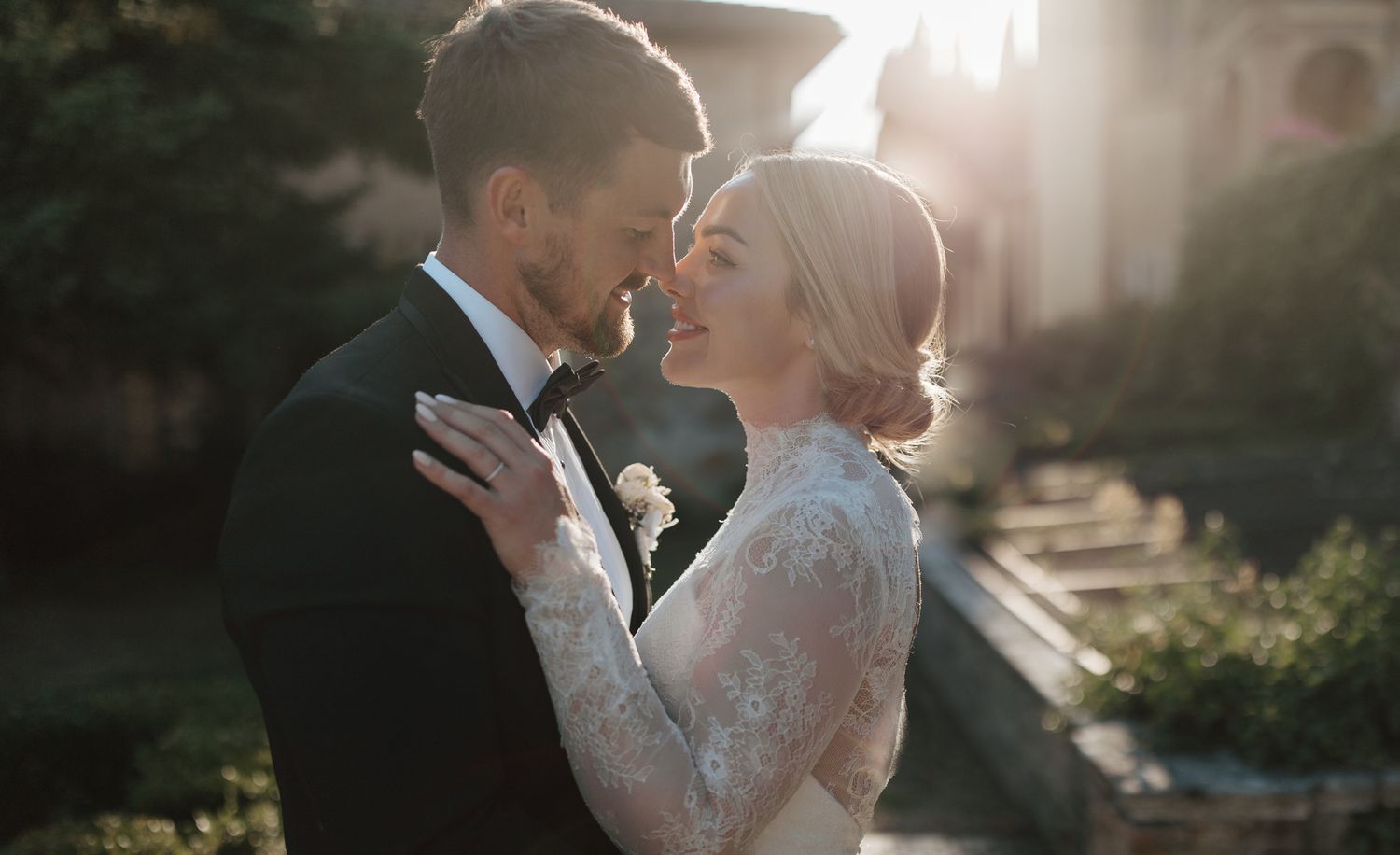 Romantic sunset wedding portraits with couple embracing against garden backdrop.