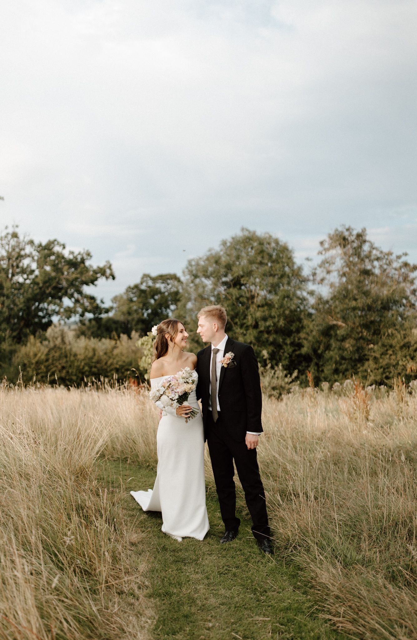 Wedding couple walking through tall grass in a natural field setting.