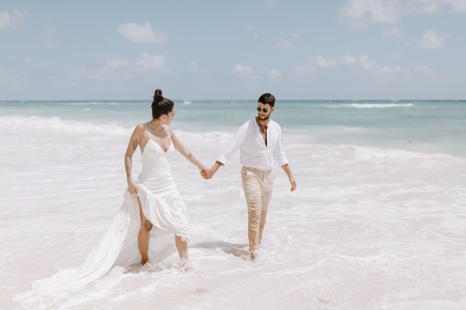 A couple walks hand in hand along a pristine white sand beach with turquoise ocean waves in the background.