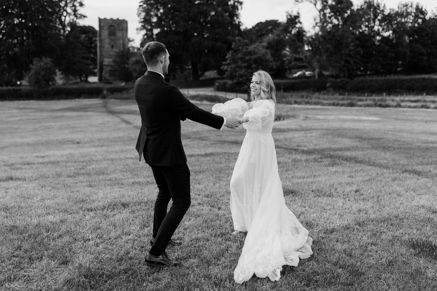 Black and white photo of couple dancing joyfully in an open field.