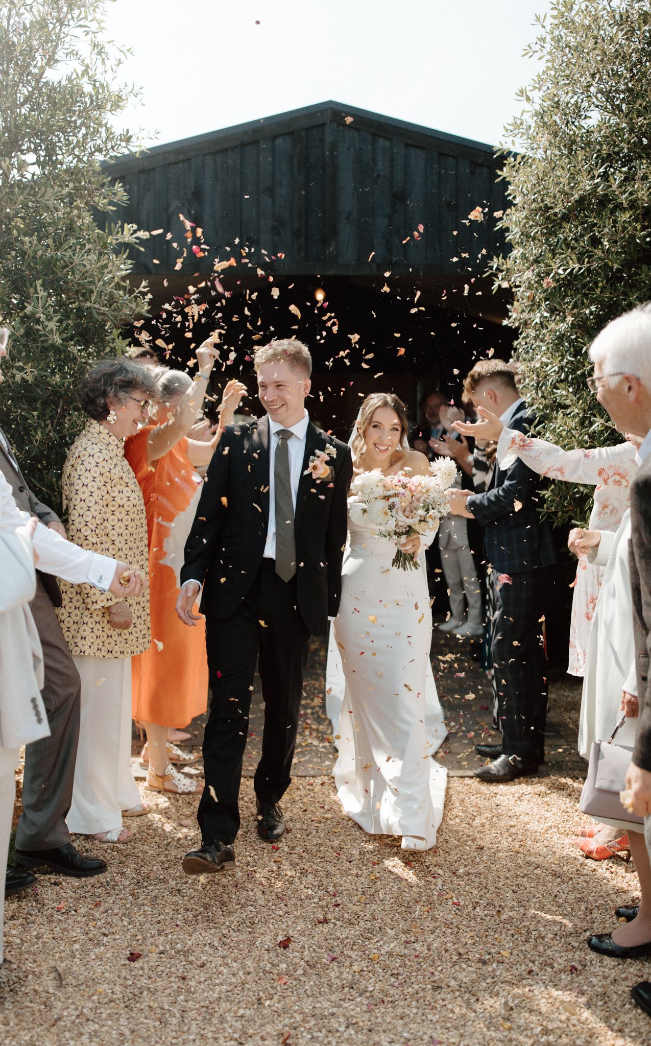 Wedding guests throw confetti in celebration along a garden pathway.