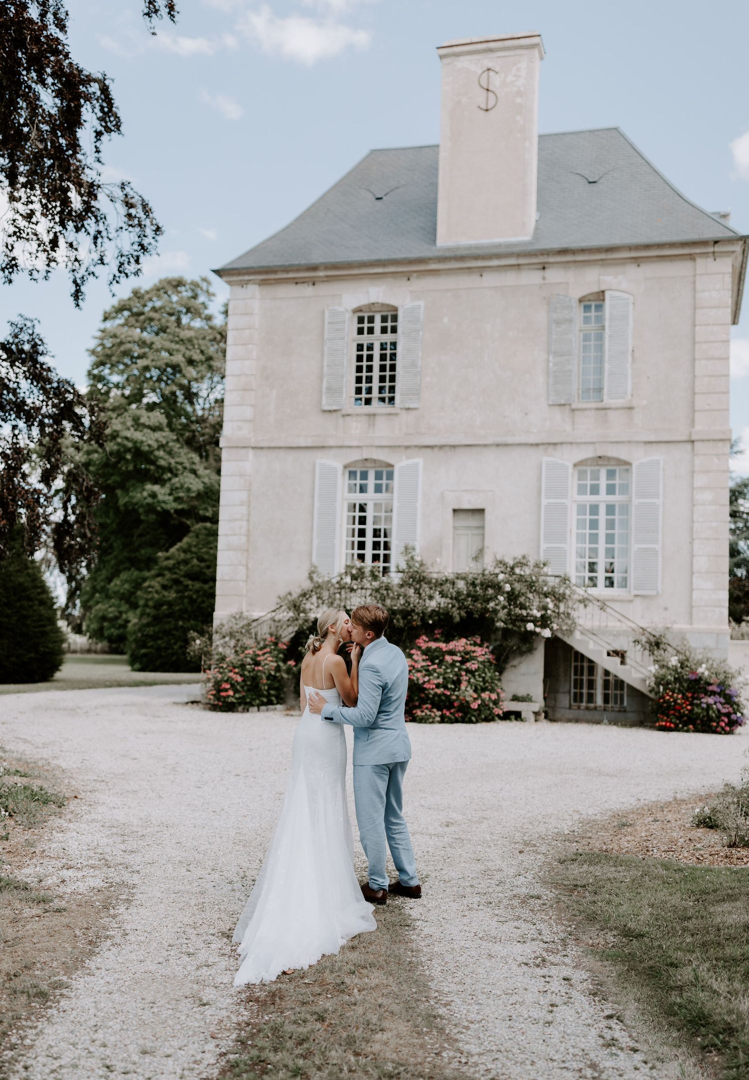 Elegant white French chateau with climbing roses and a gravel driveway.