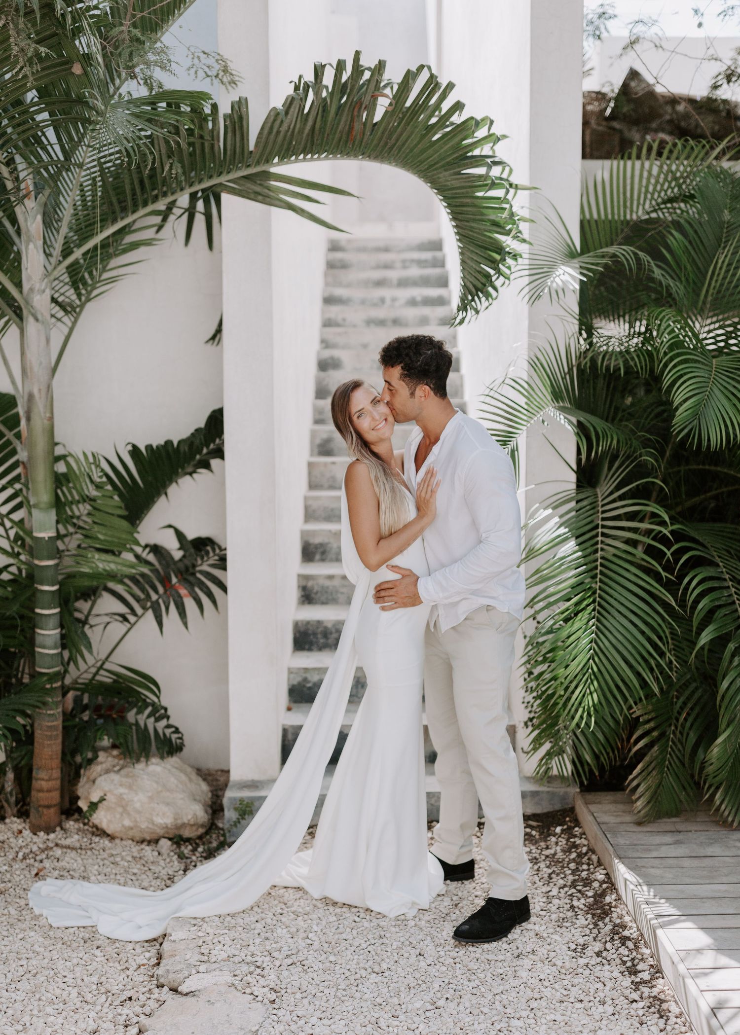 A romantic moment captured in a white columned courtyard with tropical palm plants.