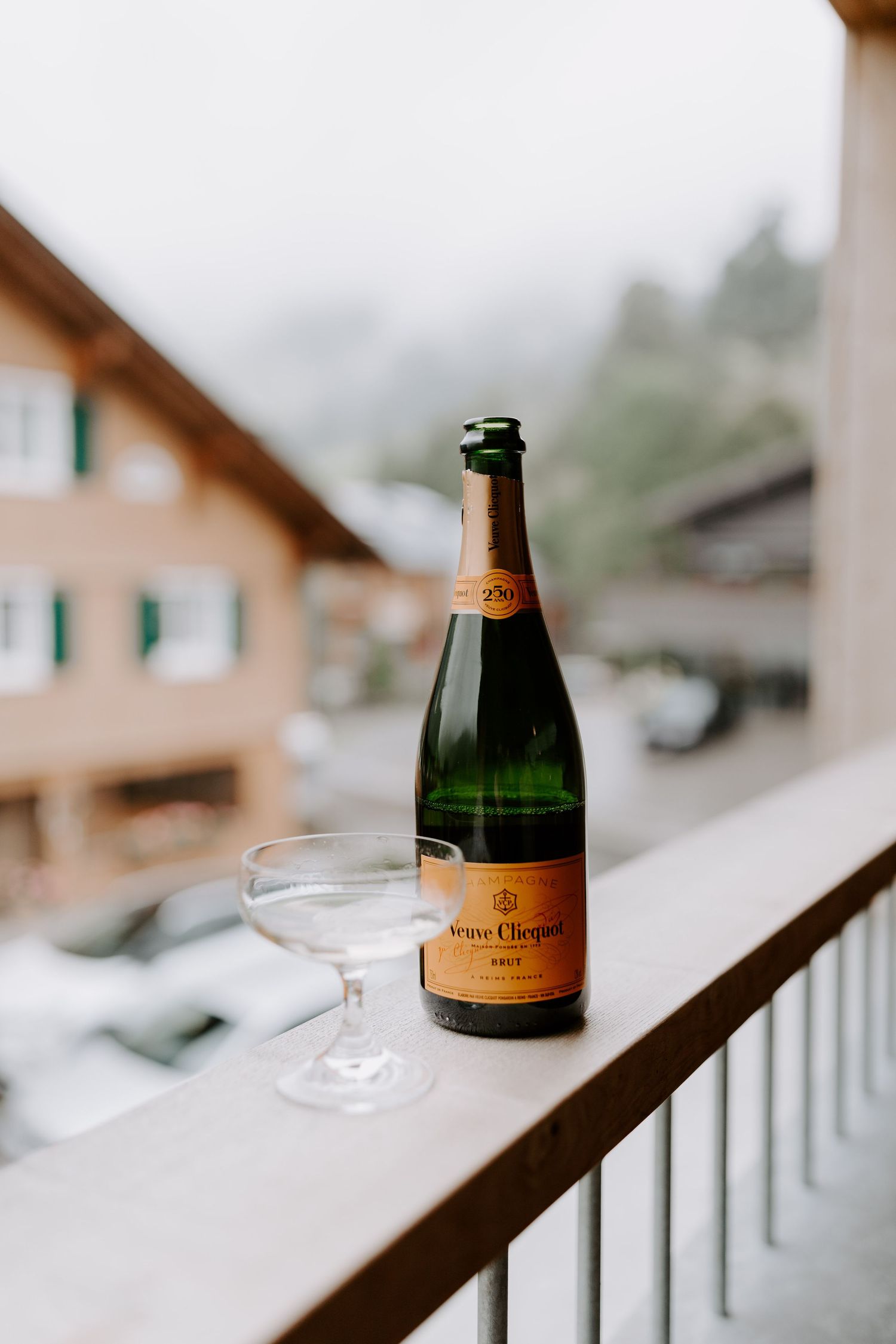Bottle of Veuve Clicquot champagne and empty glass on a balcony railing with mountain views in background.