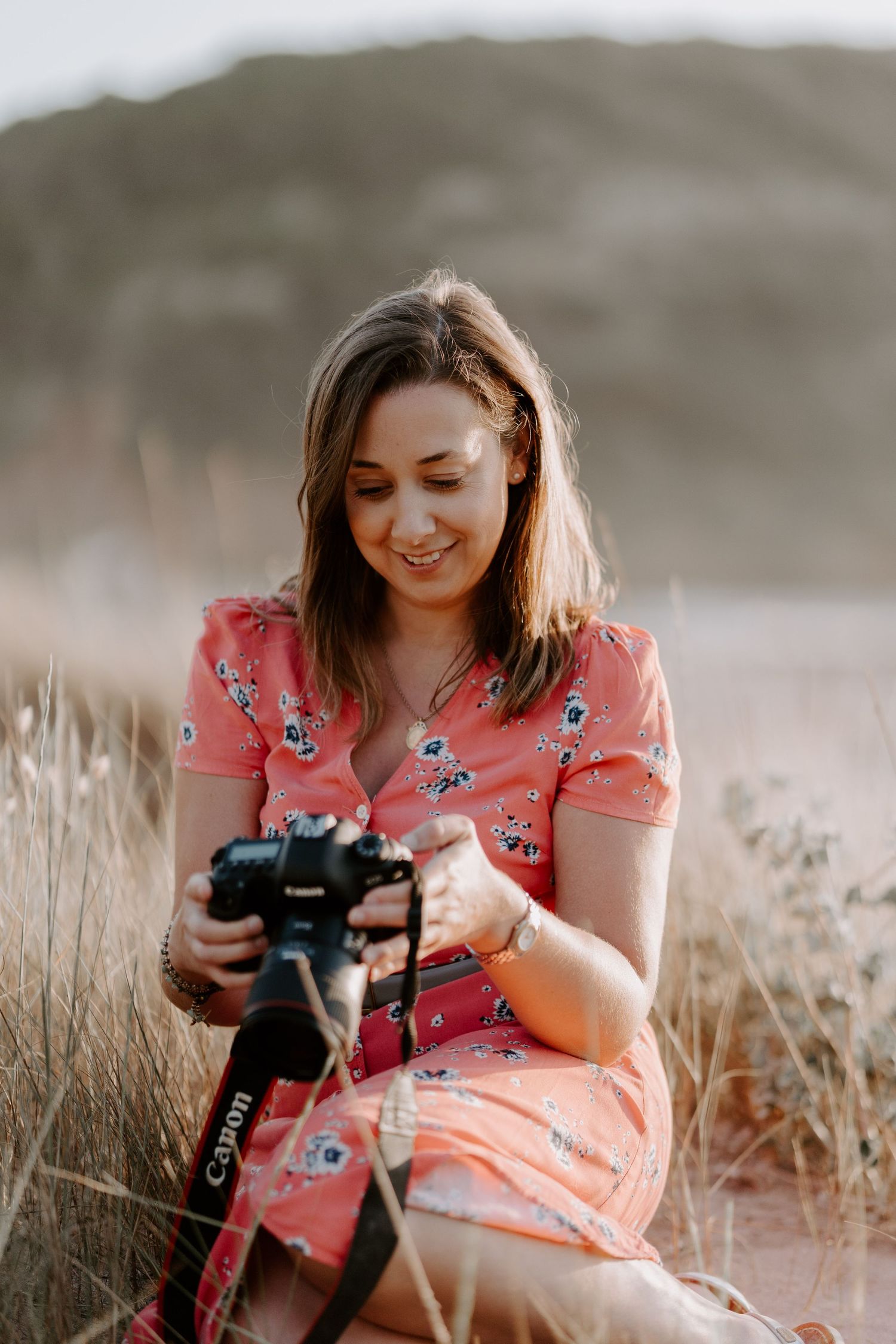 Person in floral dress looking down at camera while sitting in golden field.