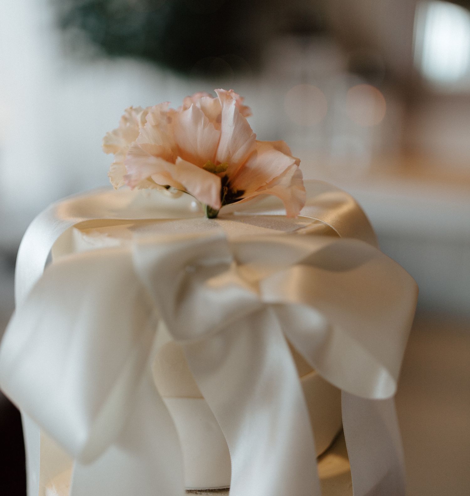 White wedding cake with delicate peach-colored bow decorations on multiple tiers.