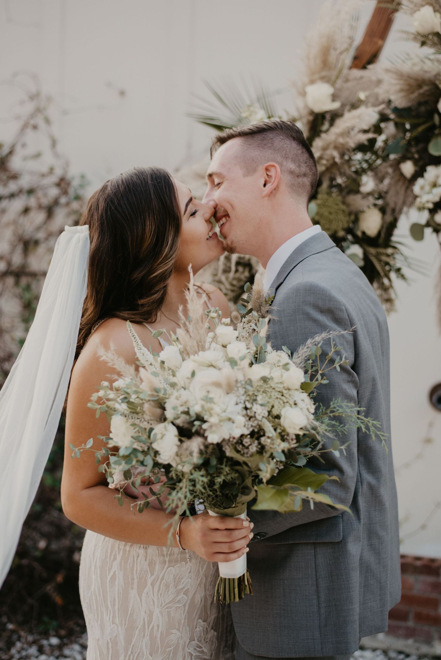 Bride and groom embracing outdoors with elegant bouquet, captured in a romantic, documentary-style by Willow + Vine Photography