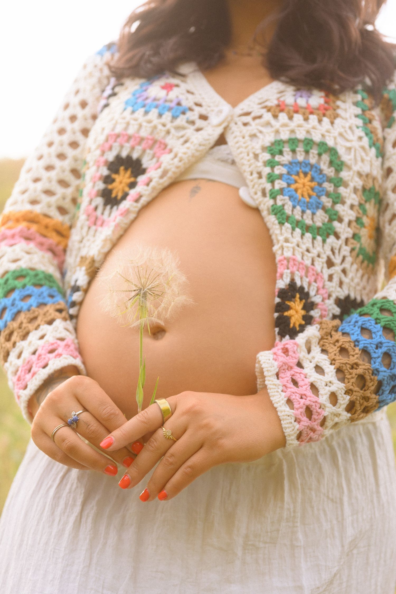 Artistic maternity detail shot holding a dandelion against crochet sweater.